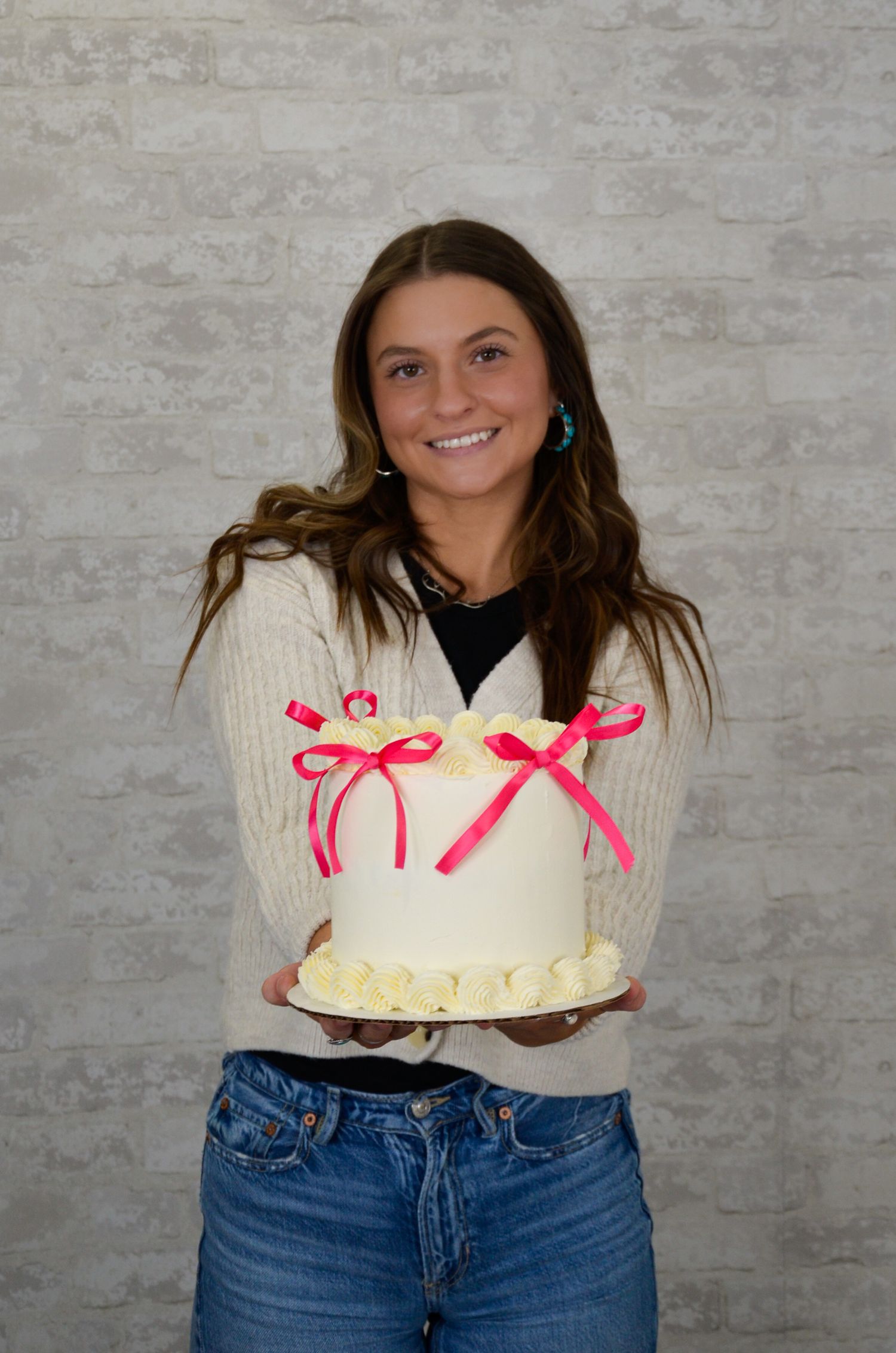 Person in cream sweater with pink bows poses against textured wall.