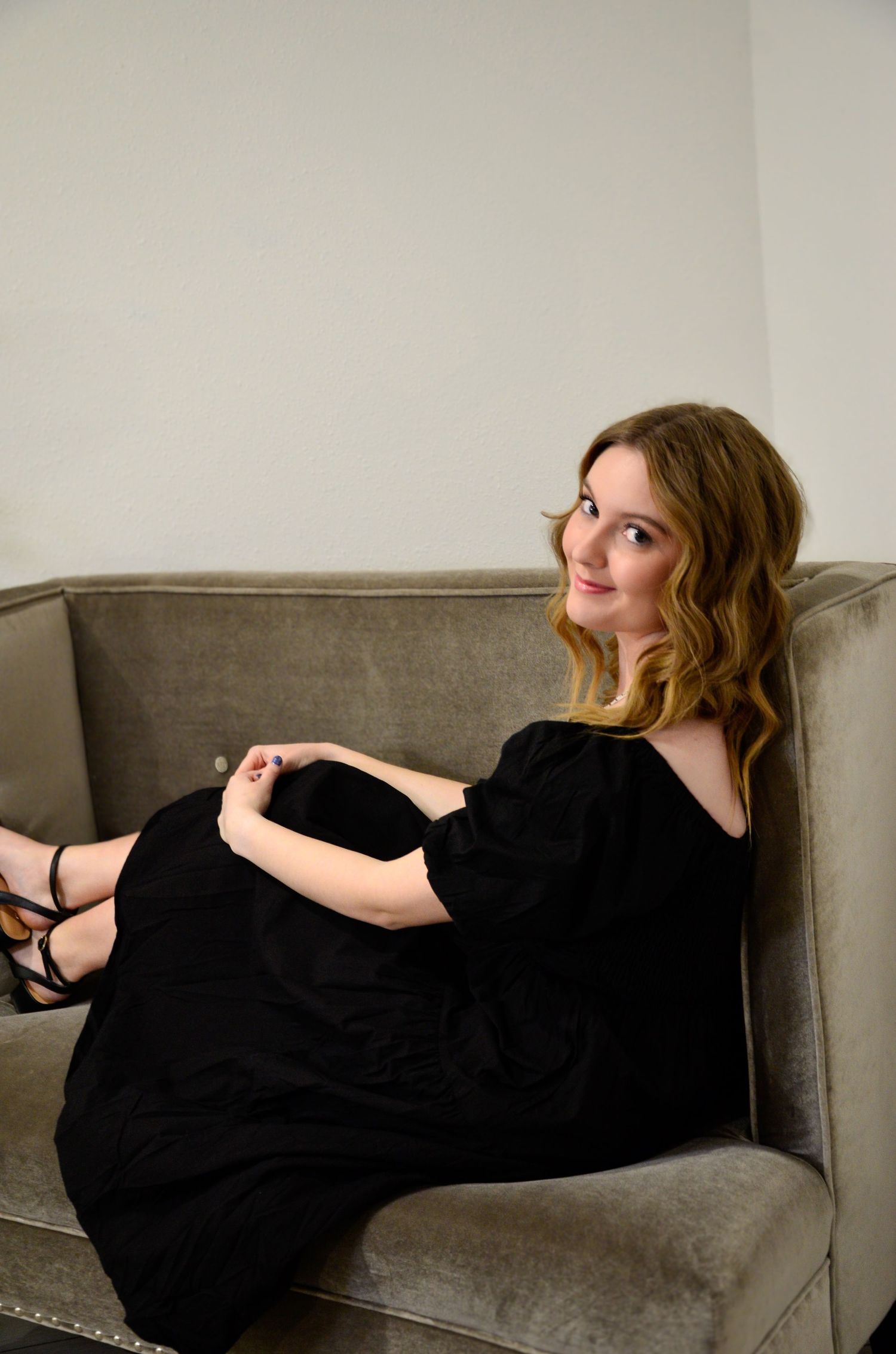 Person in black dress reclines elegantly on gray couch.