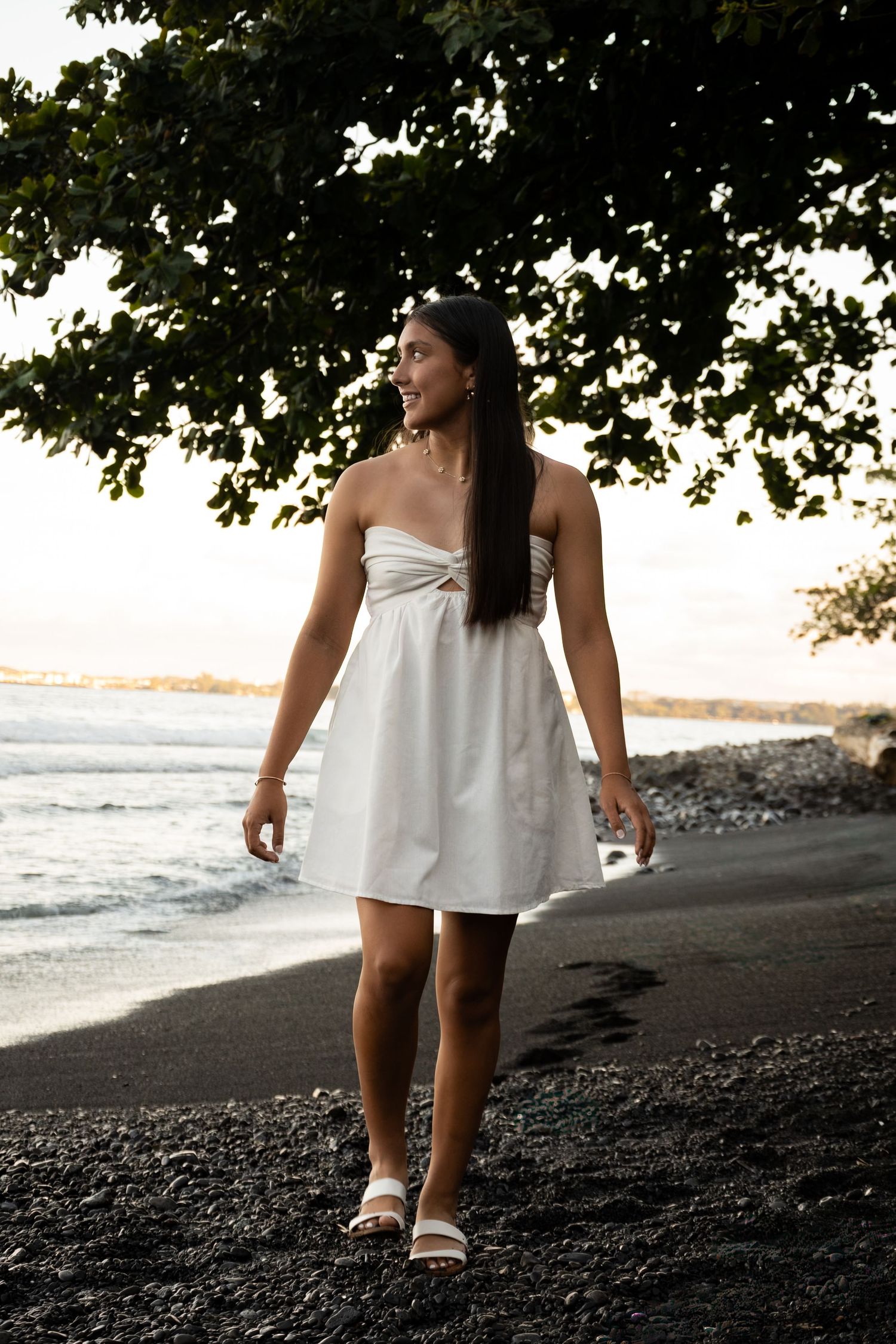 Figure strolling along volcanic black sand beach with waves and tropical foliage visible.