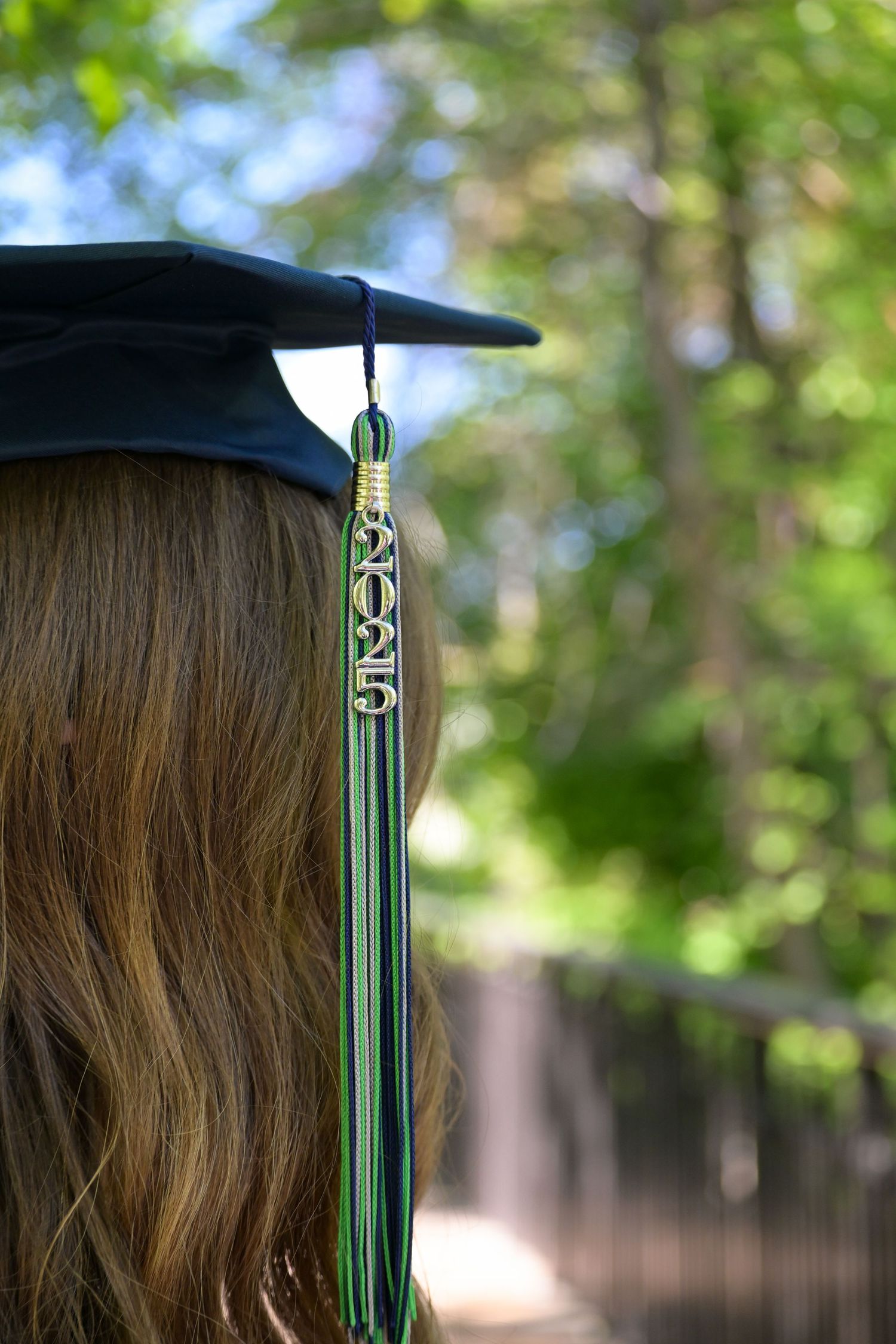 Close-up view of a green graduation tassel with 2023 charm hanging against a blurred natural background.