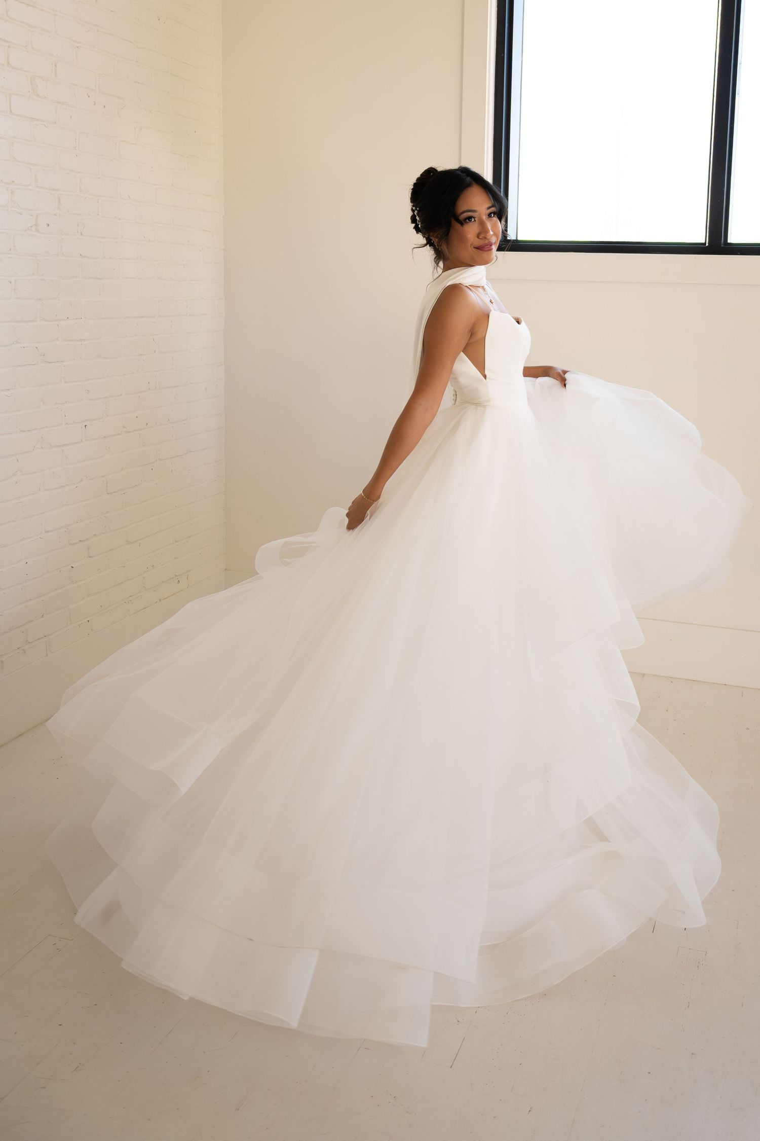Bride twirling in a voluminous layered white tulle ball gown in a bright studio space.