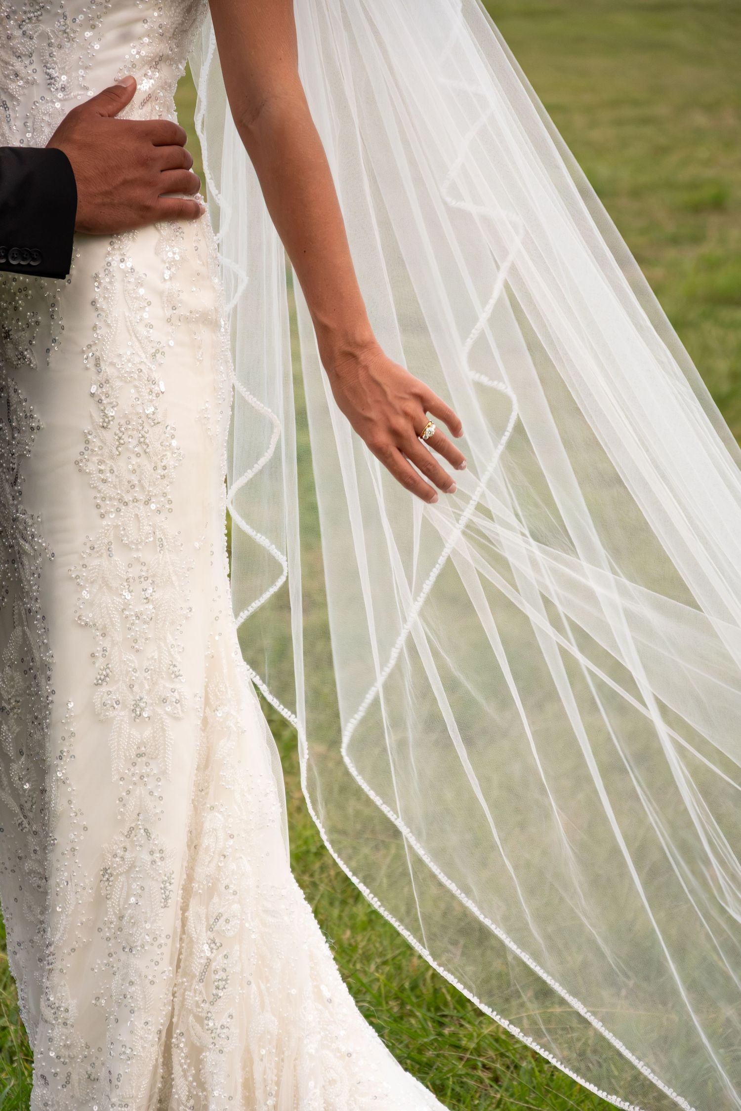 Close-up of bride's lace wedding dress and flowing veil with diamond ring visible on her hand.