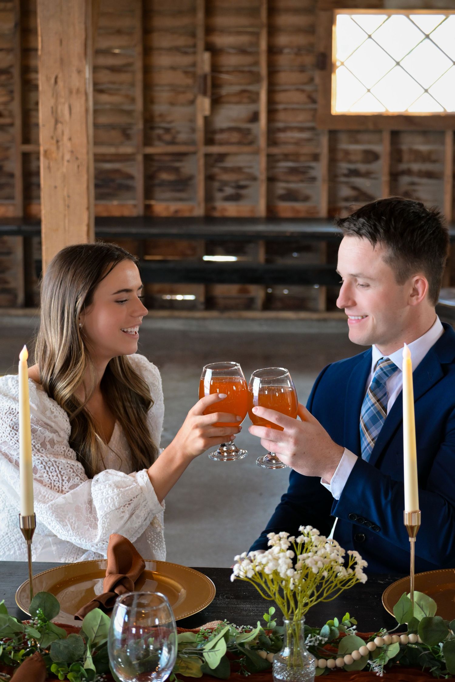 Couple toasts with amber drinks at rustic wedding reception with floral table decor.
