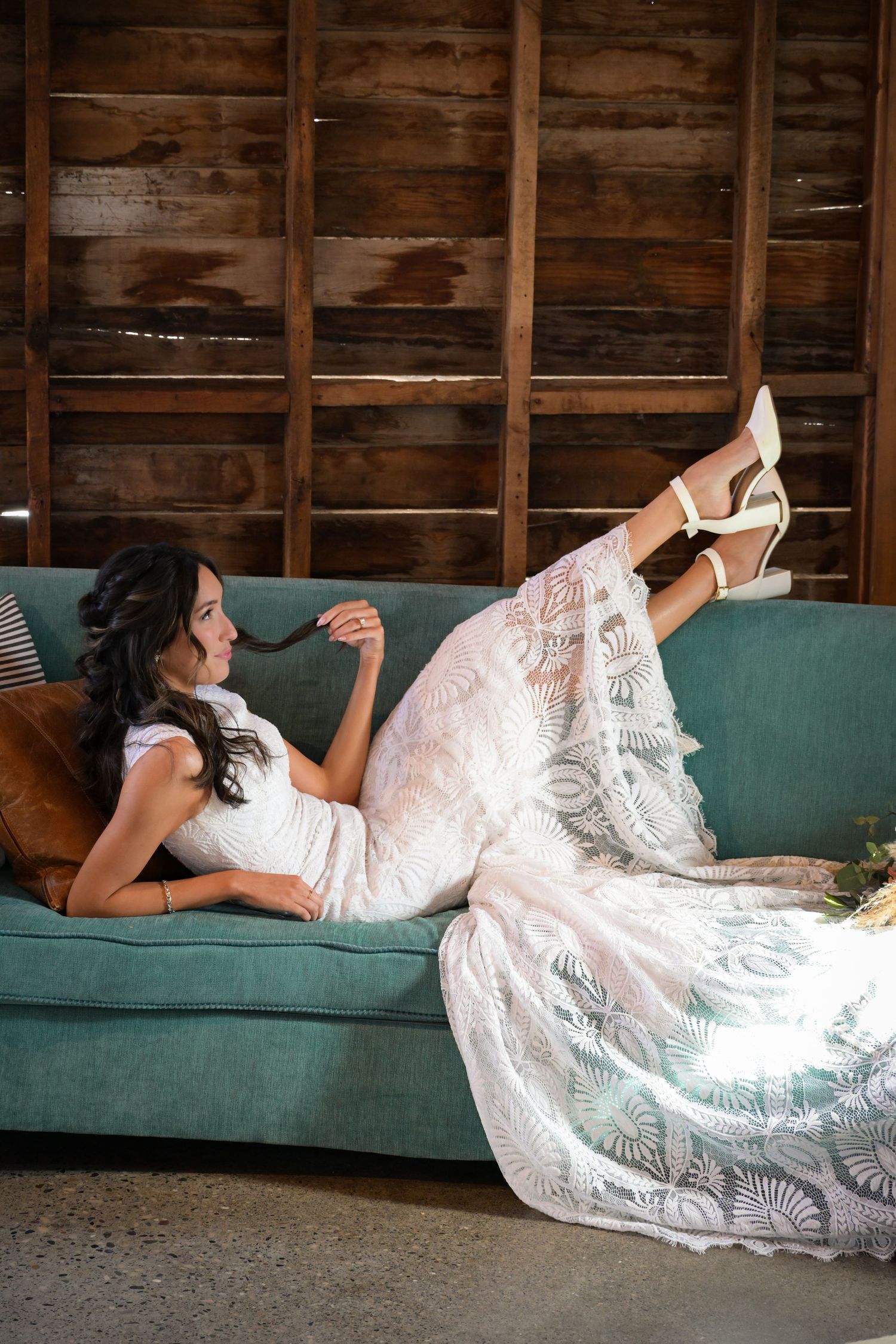A bride in lace wedding dress poses elegantly on a green velvet couch.