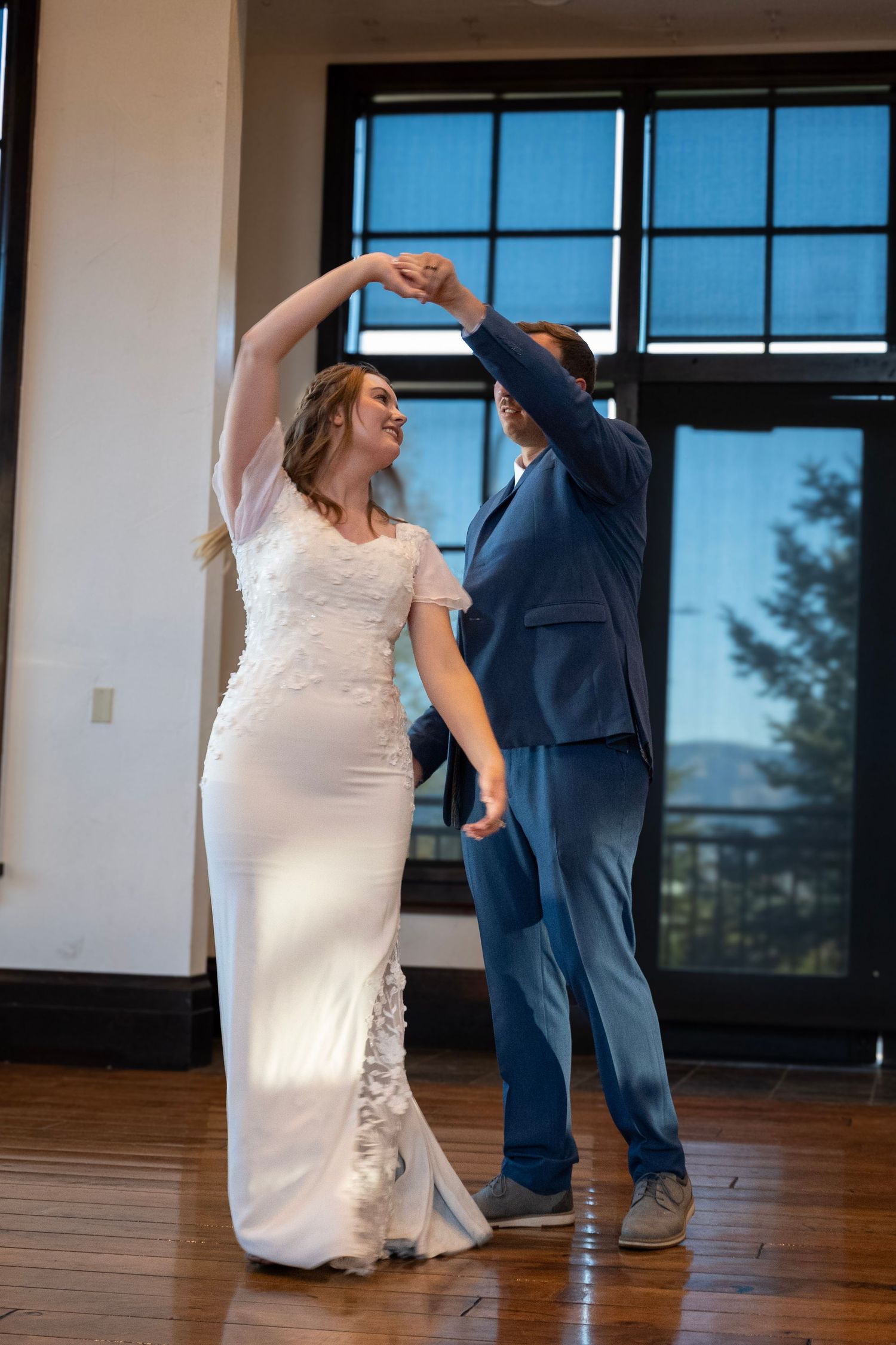 A couple dances together in a sunlit room with large windows and wooden floors.