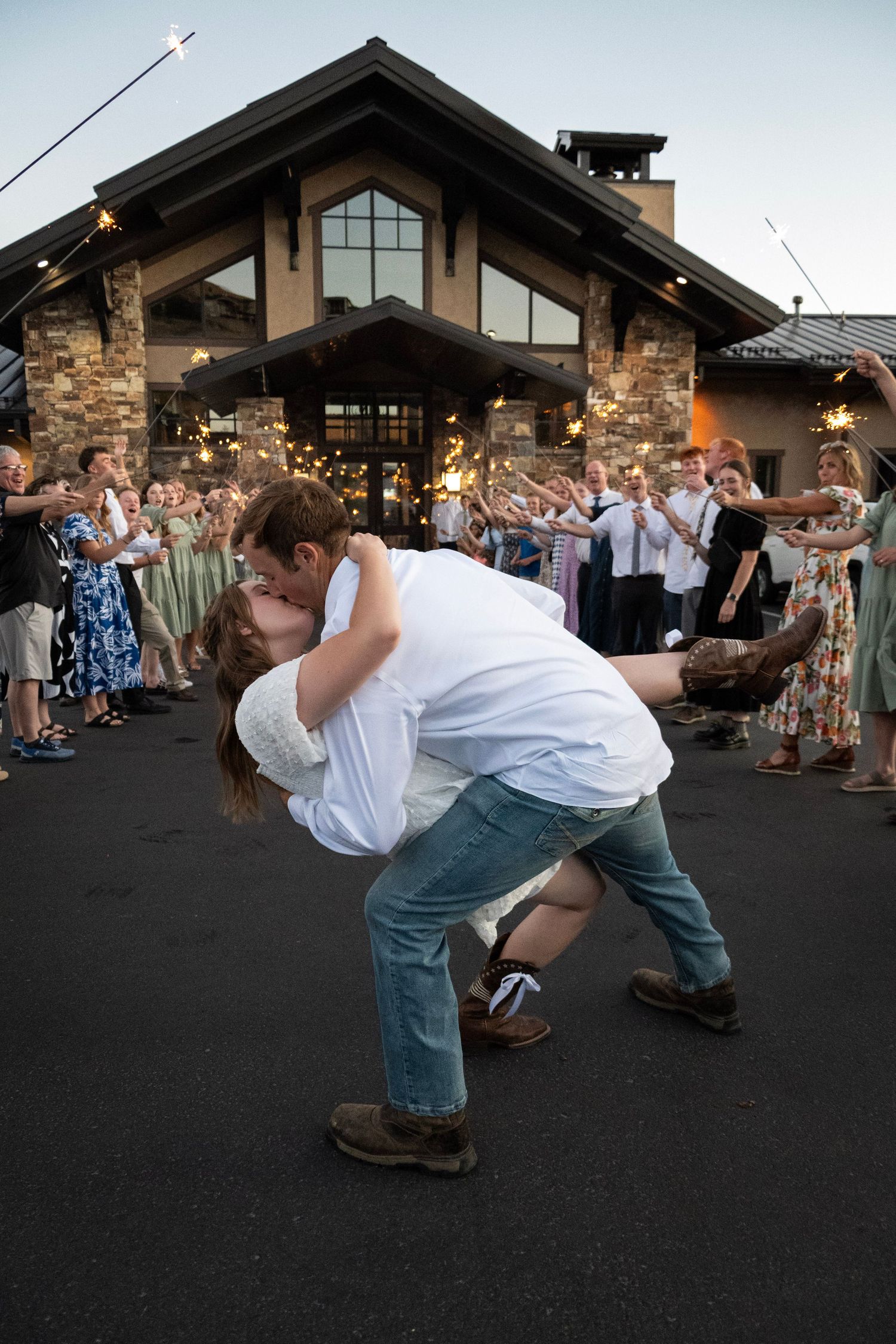 A couple performs a synchronized dip dance move at an outdoor venue with string lights and stone walls in the background.