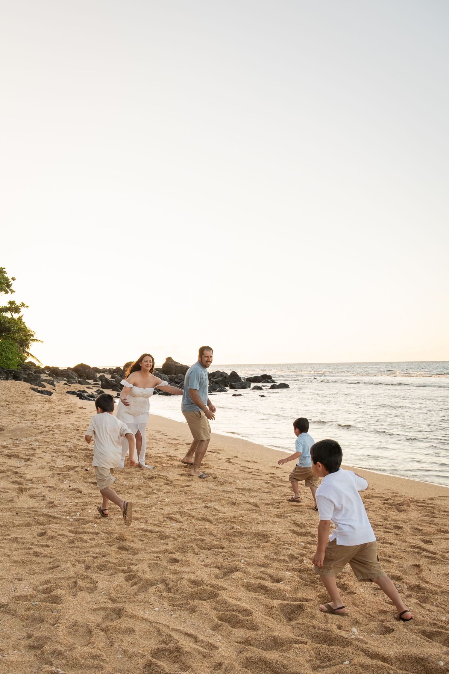 Family playing on a sandy beach at sunset, with children running toward their parents near the ocean.