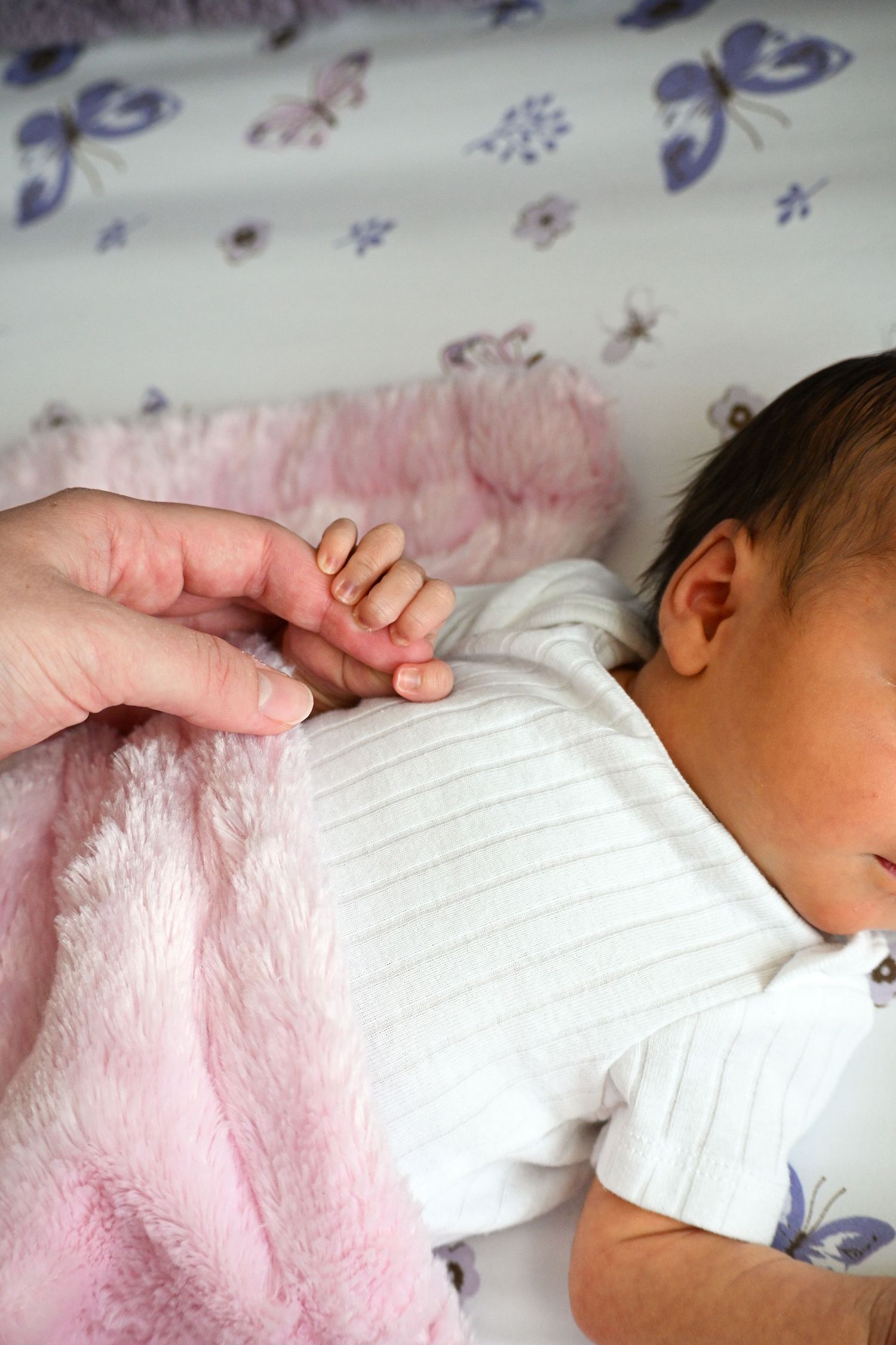 Gentle touch between adult and baby hands on floral patterned bedding.