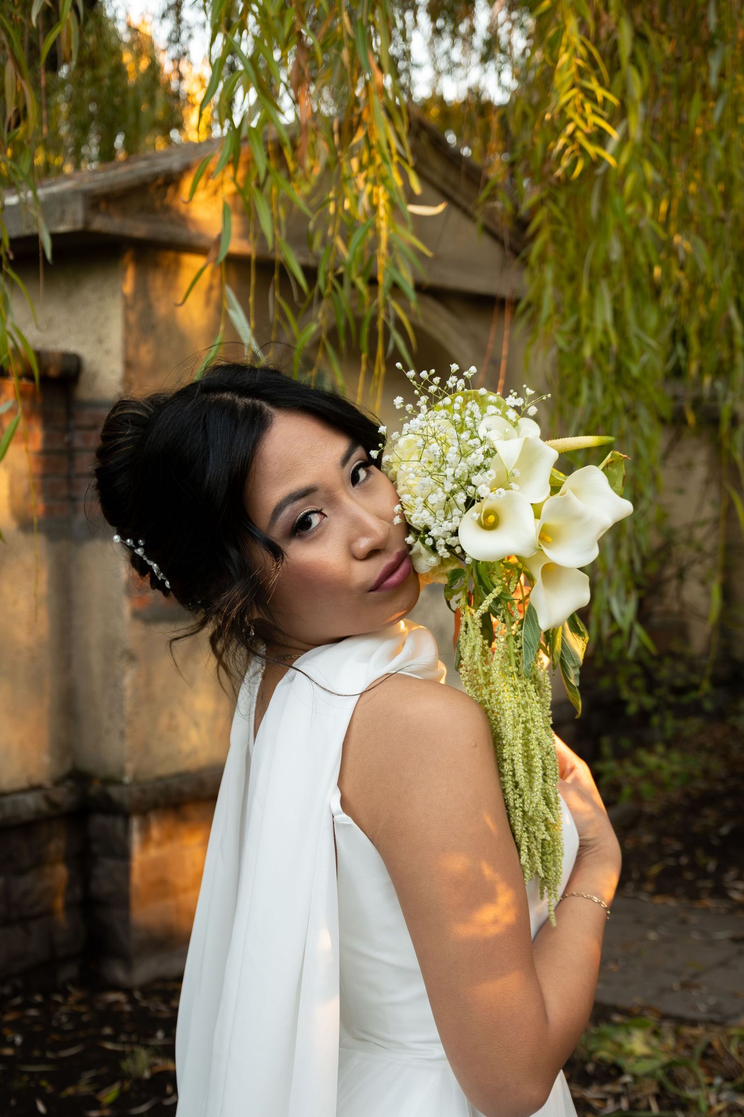 Beautiful bride in a white halter gown holding a cascading calla lily bouquet outdoors.