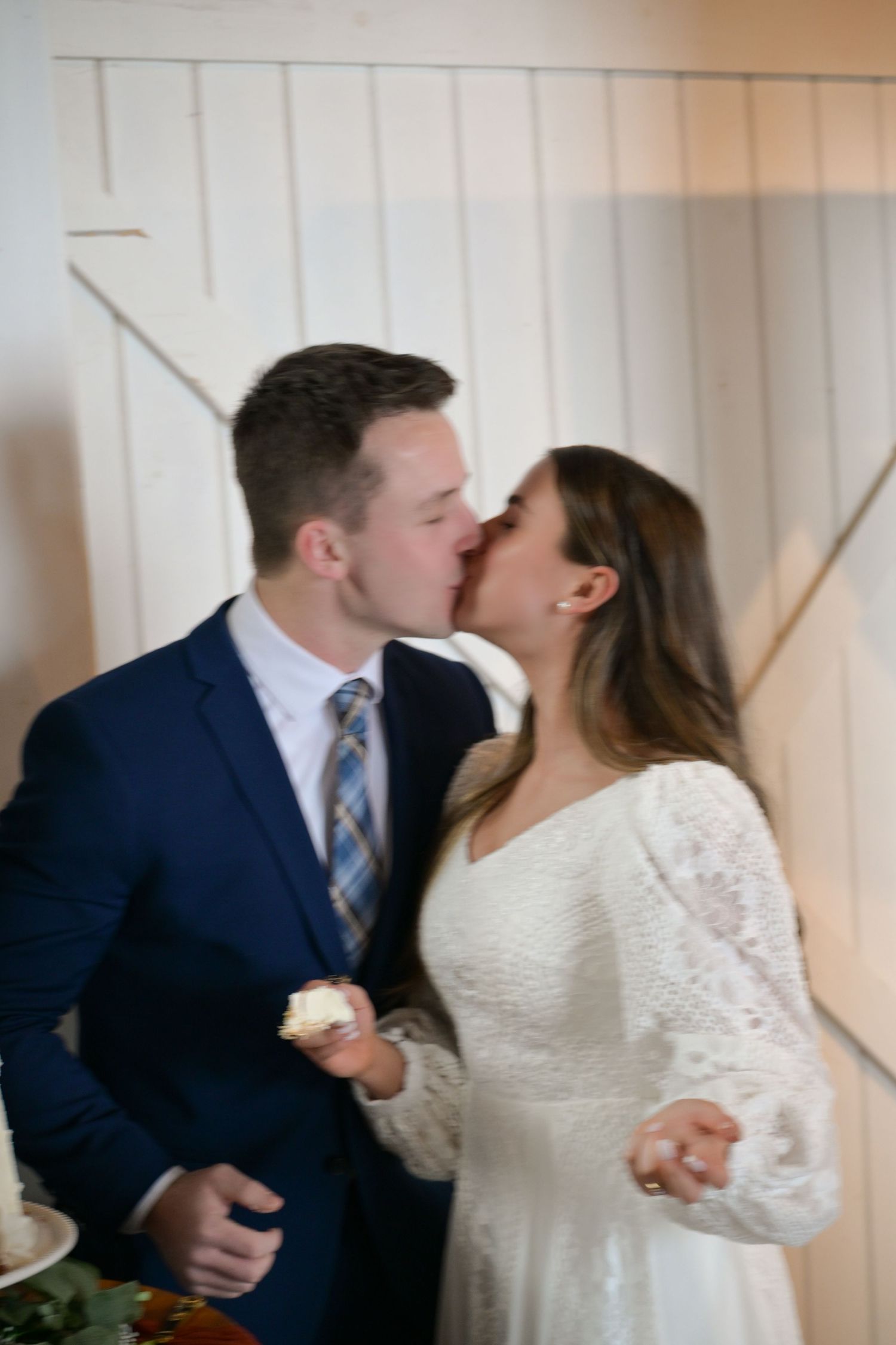 A romantic wedding couple sharing their first kiss against a white wood wall.
