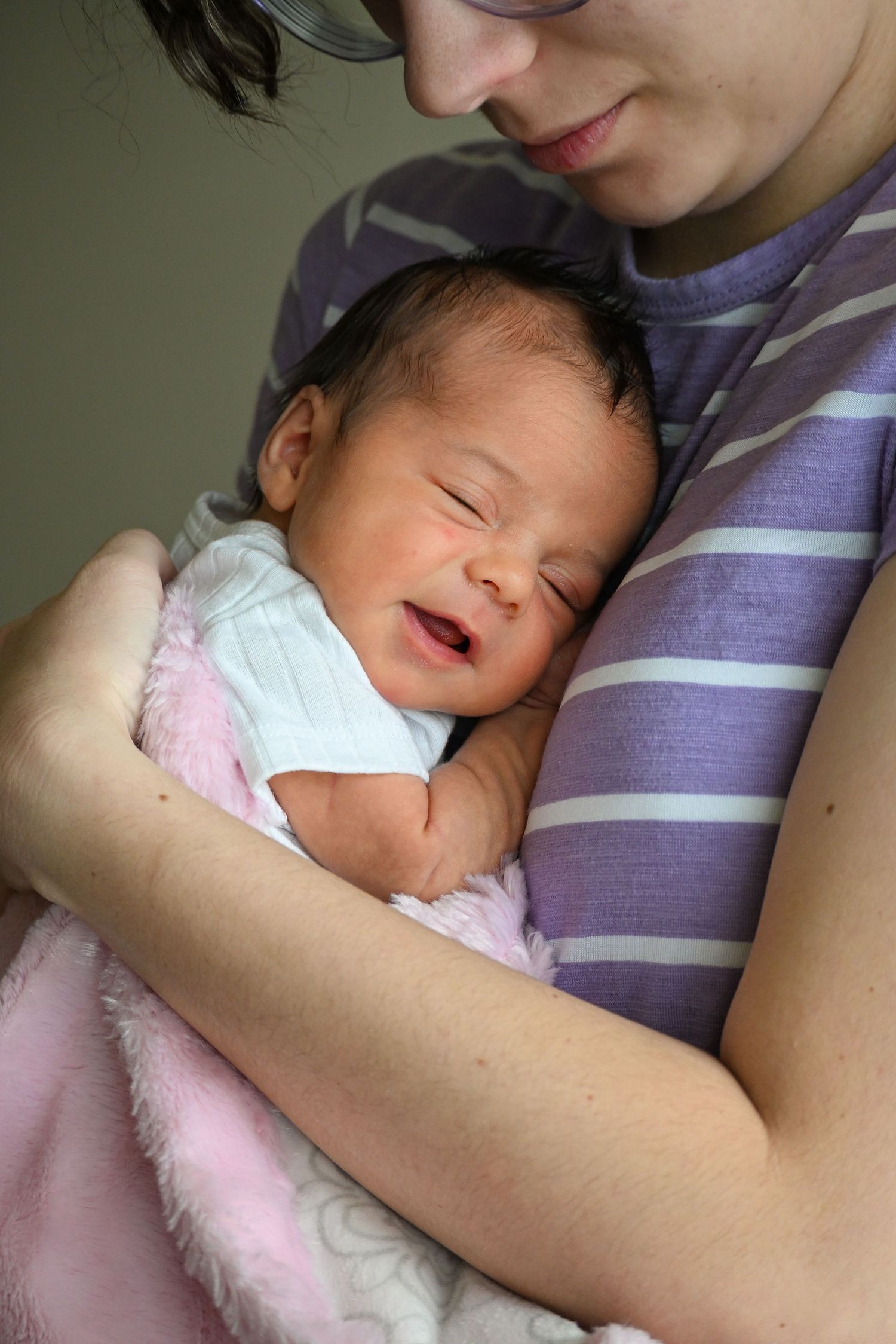 Sleeping newborn in white outfit cuddled on pink blanket.