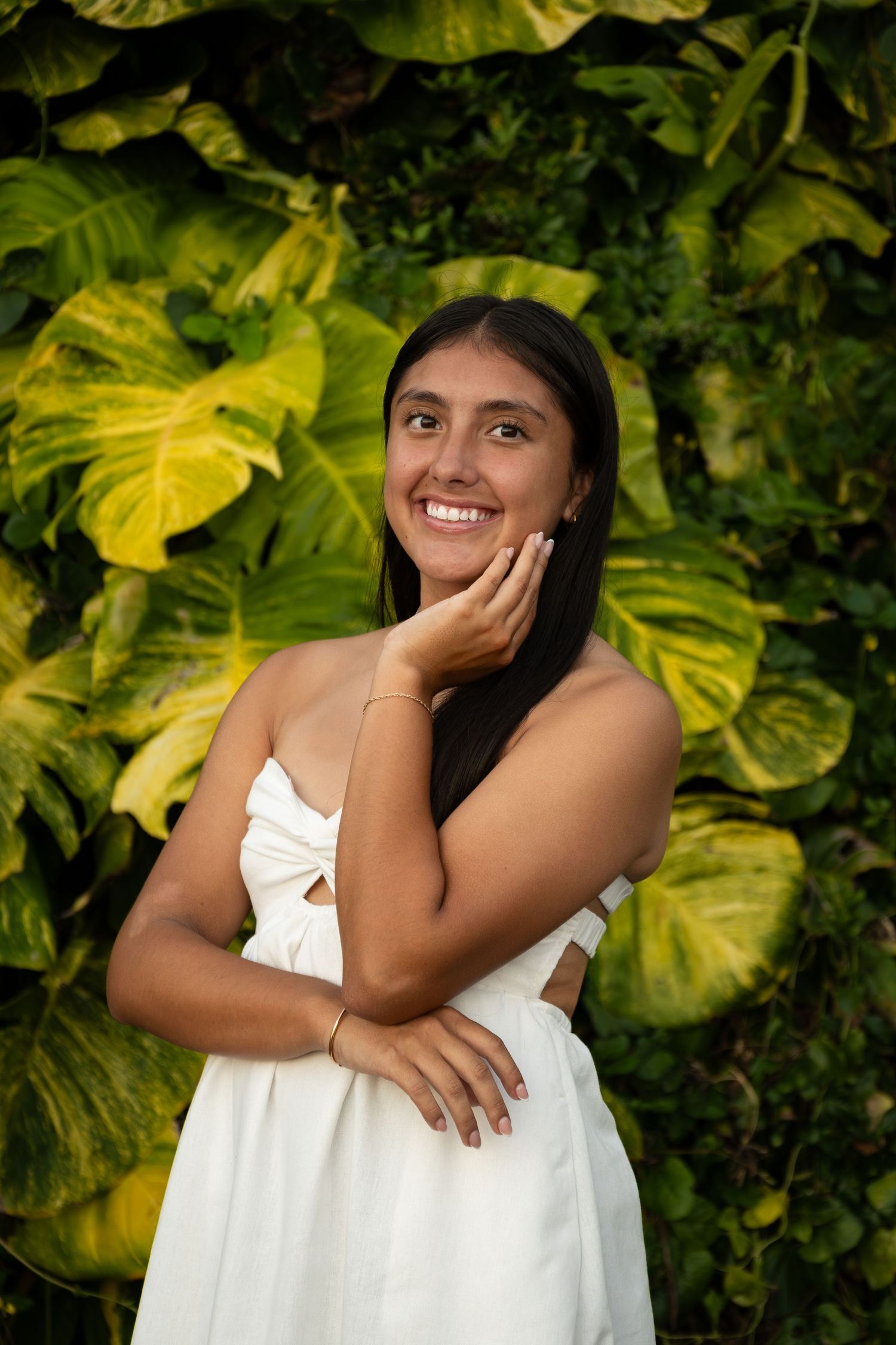 A bright portrait in a white dress against lush tropical foliage with large yellow-green leaves in the background.