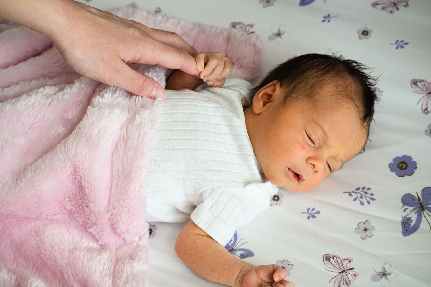 Peaceful sleeping infant wrapped in pink blanket on floral patterned bedding.