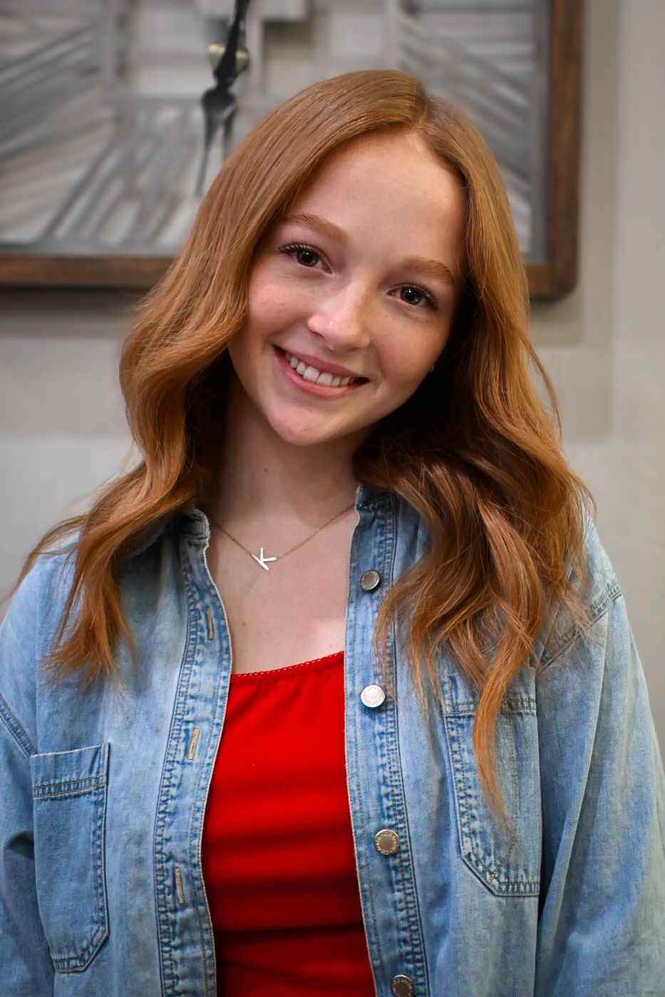 Person in denim jacket and red top smiles warmly indoors.