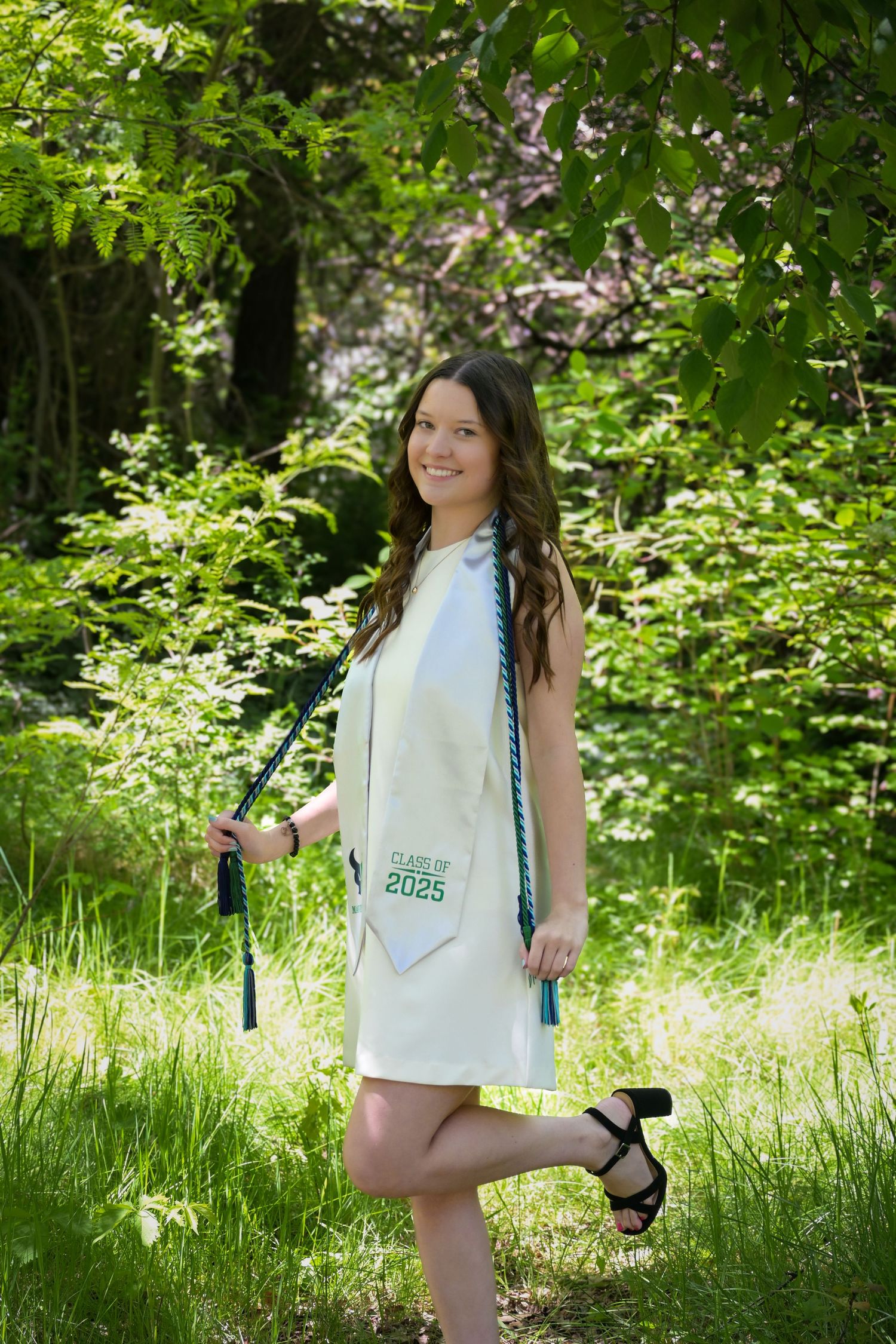A person in a white dress carries a reusable shopping bag while walking through lush green summer foliage in a garden setting.