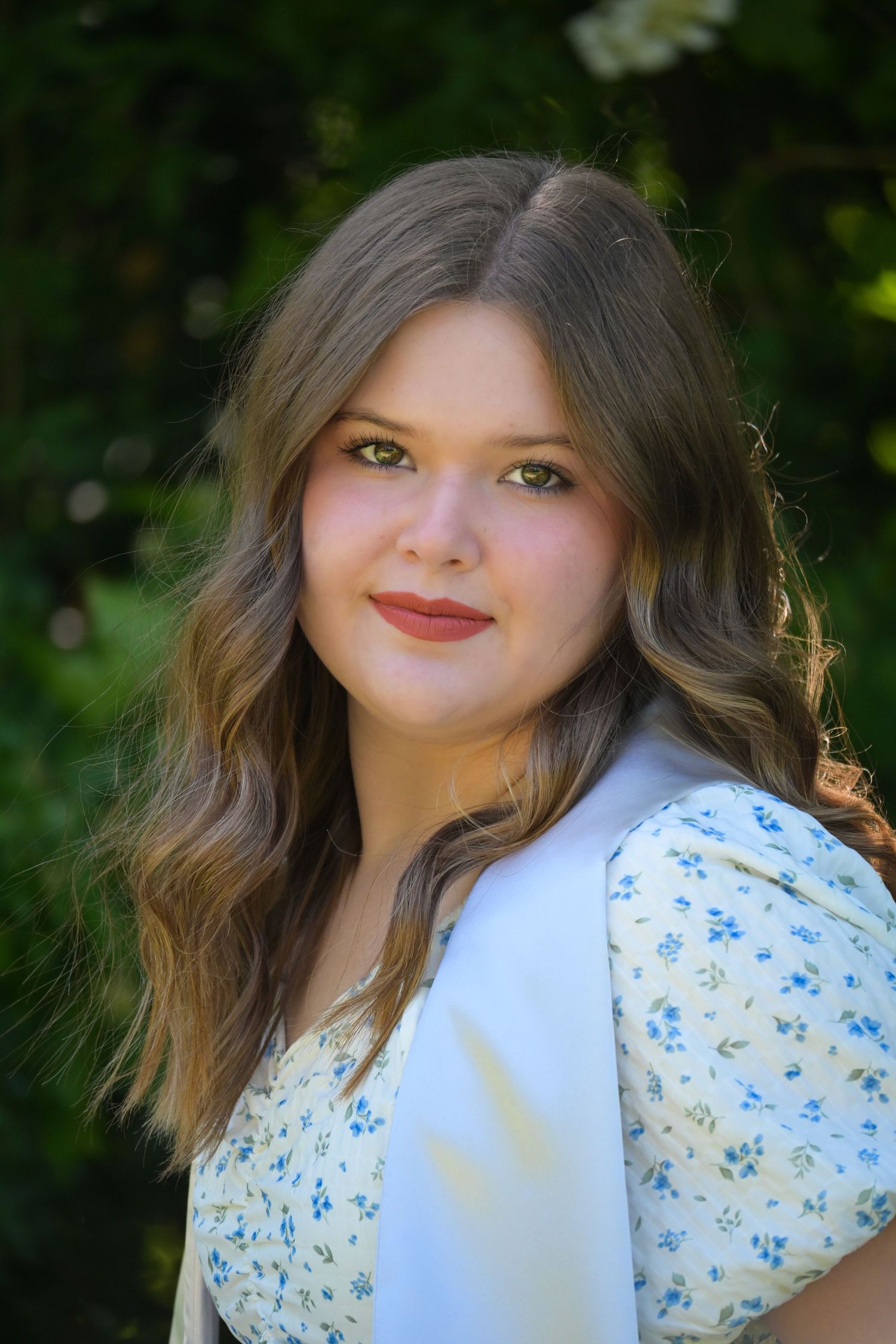 Portrait in white floral dress against natural green background with soft lighting.