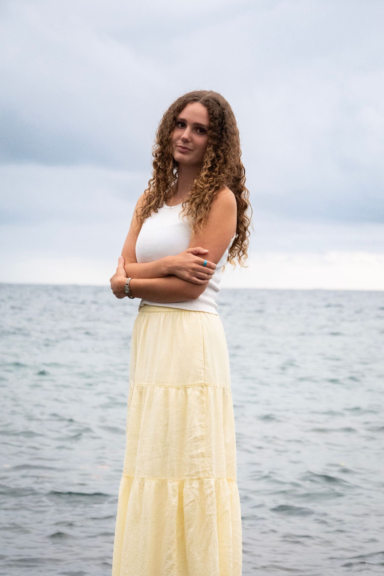 A yellow tiered maxi dress is showcased against a moody ocean landscape on an overcast day.