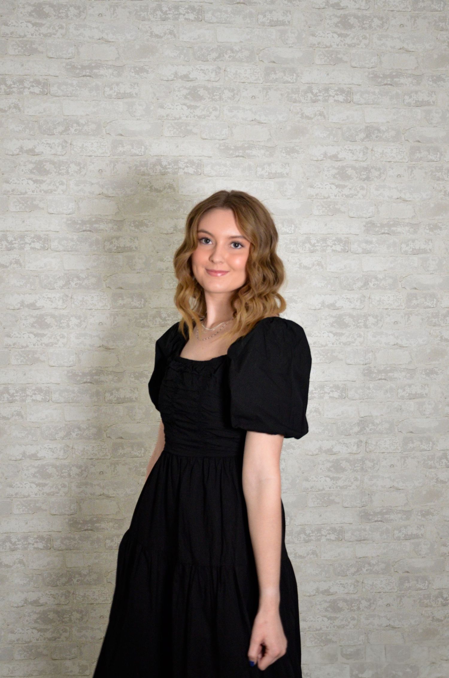 Person in black puff sleeve dress poses against textured gray wall.