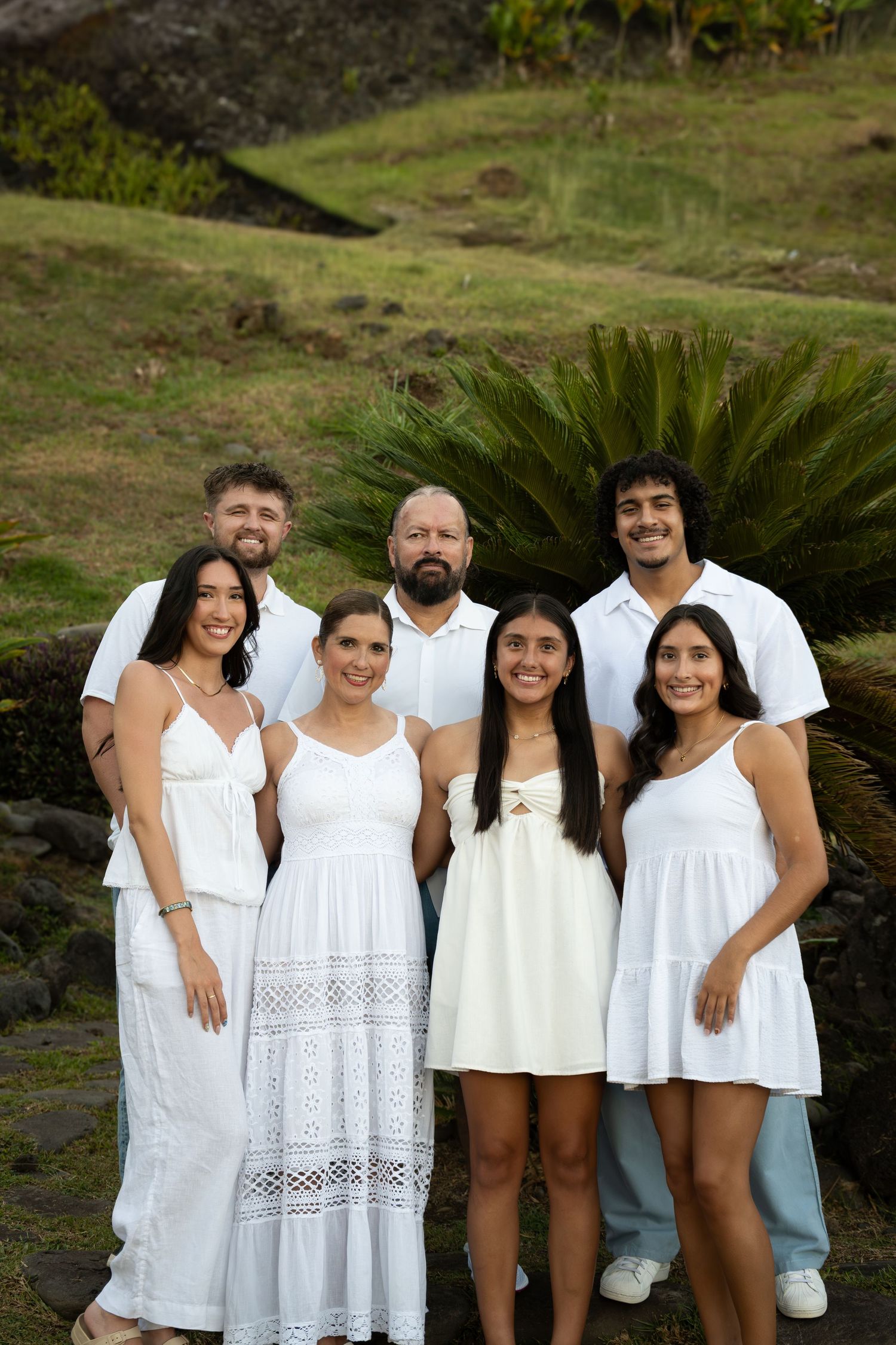 A group of people wearing coordinated white outfits pose together outdoors for a family photo session.