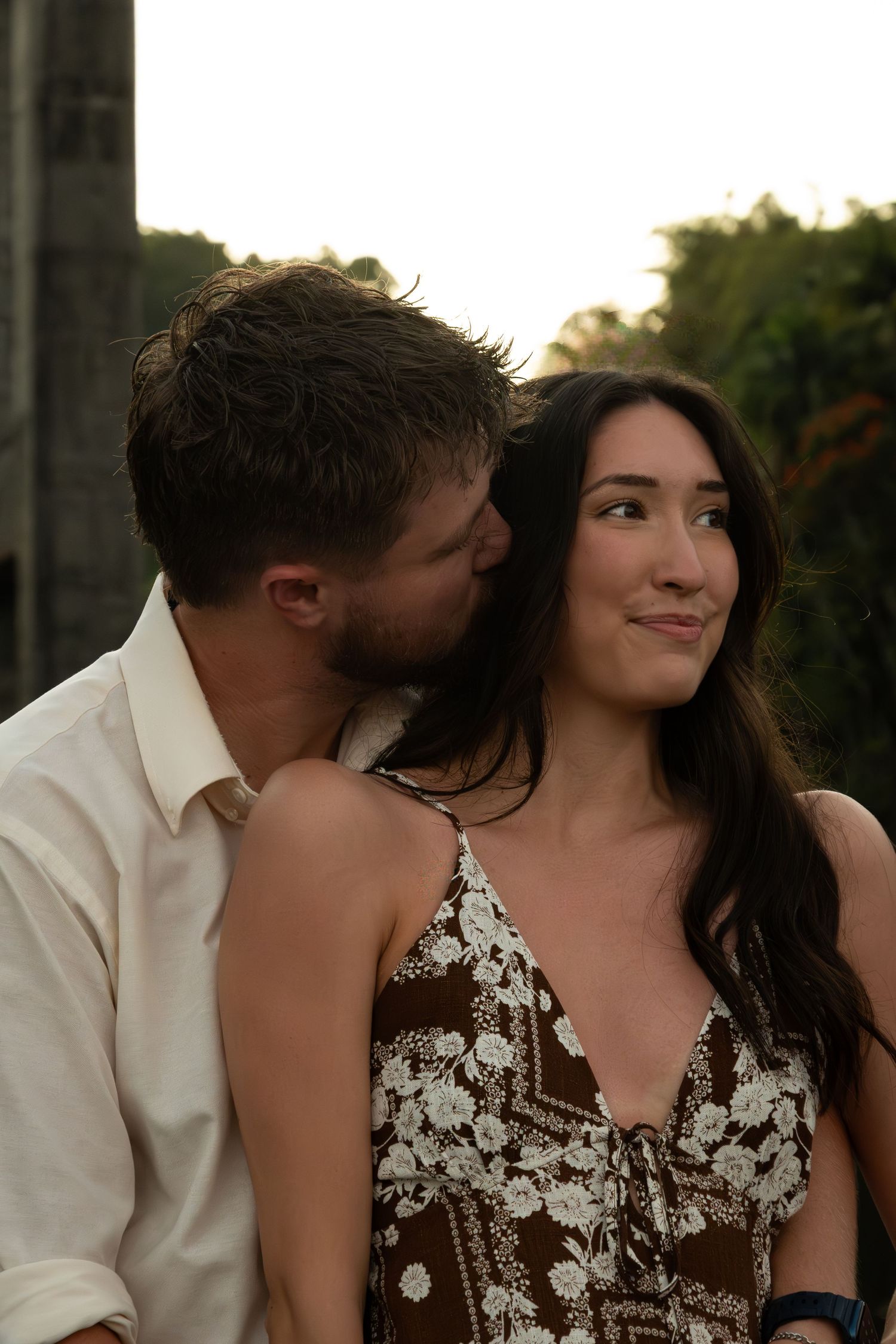 A romantic couple shares tender moments in a floral dress and white shirt against a natural outdoor backdrop.