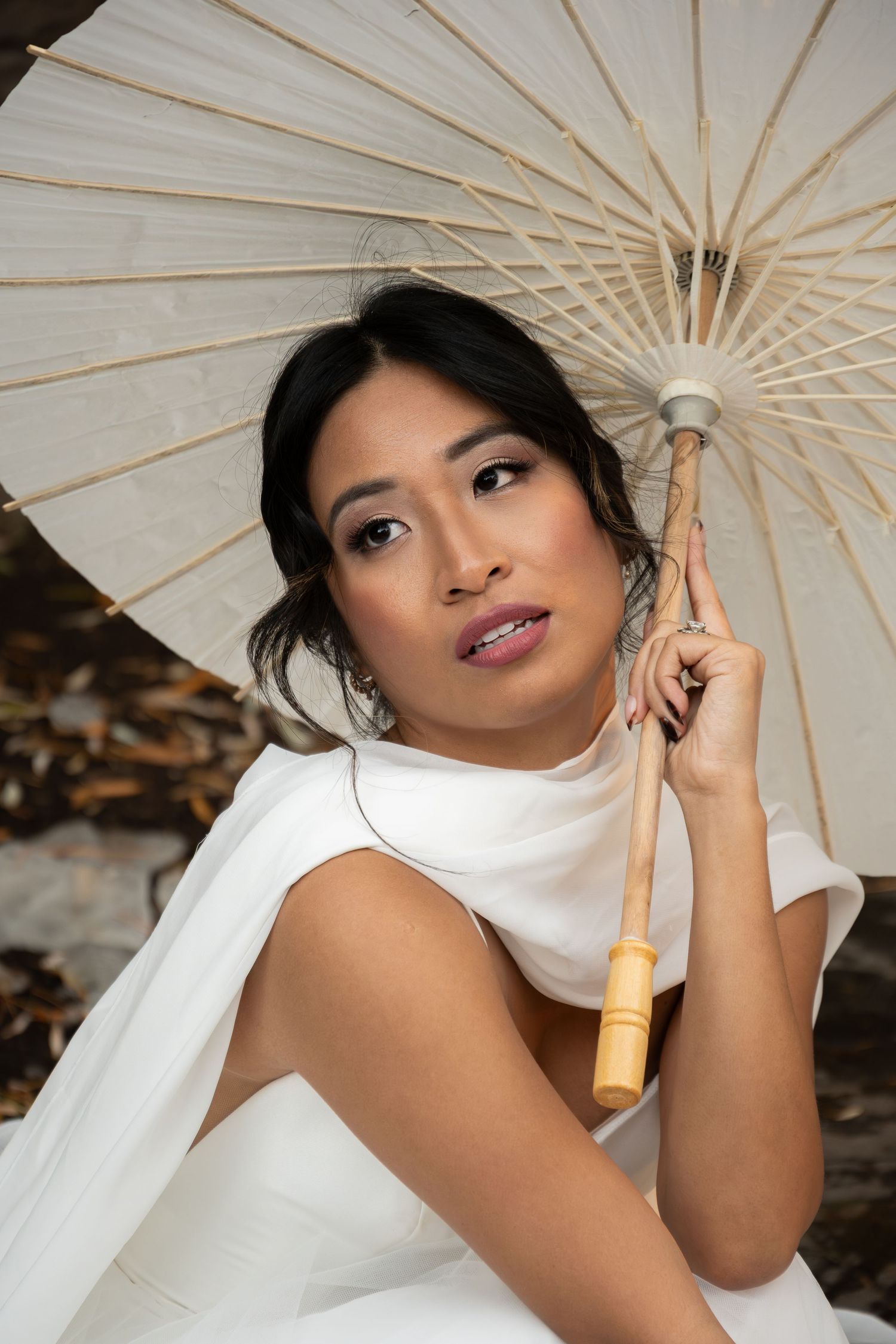 Bride in a white cape gown holding a paper parasol umbrella in an outdoor setting.