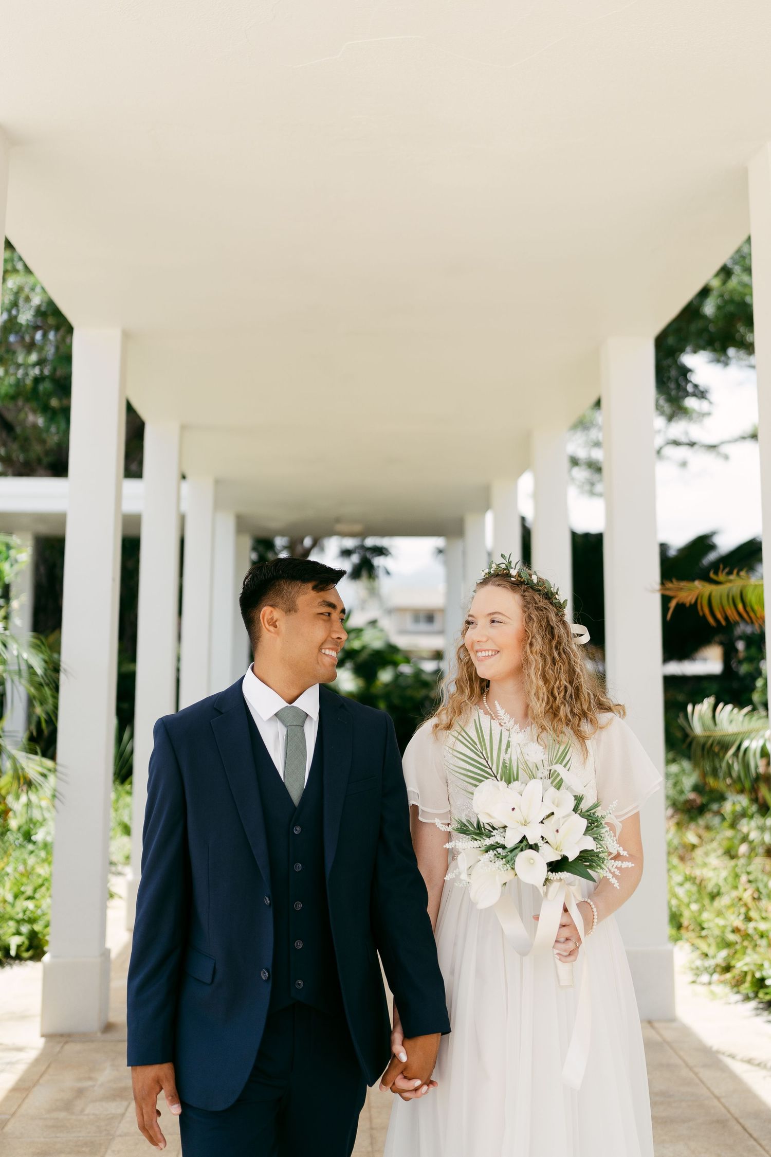A bride and groom share a loving glance while walking along a columned pathway.