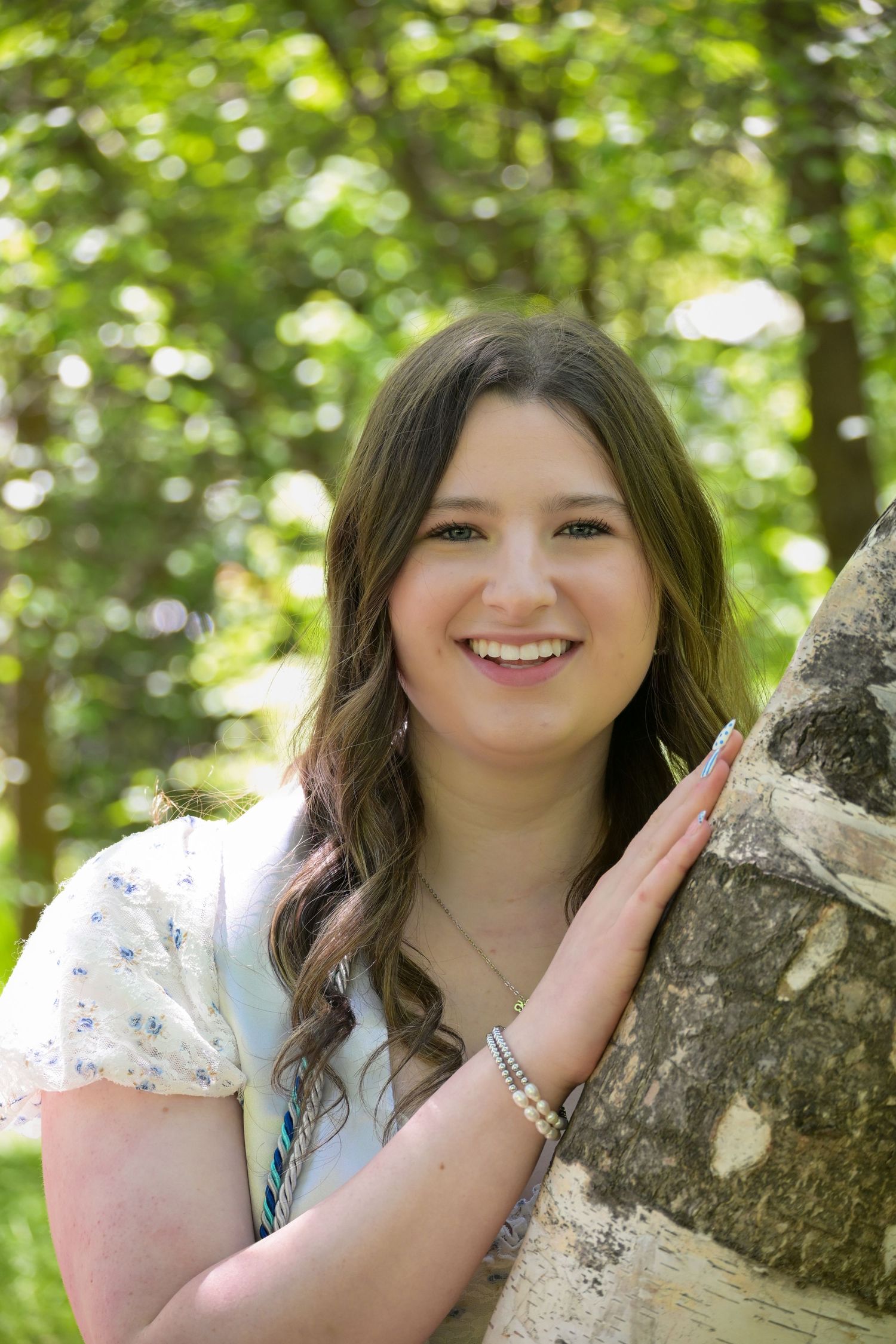 A series of outdoor portraits showing someone in a white floral dress posing against a tree trunk with greenery in background.