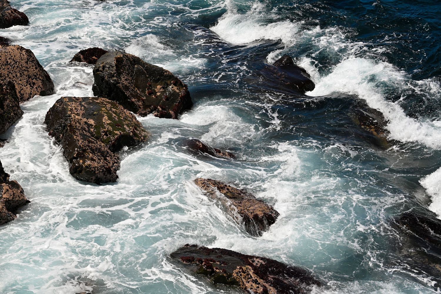 Dramatic ocean waves crash against rocky coastal formations creating white water spray.
