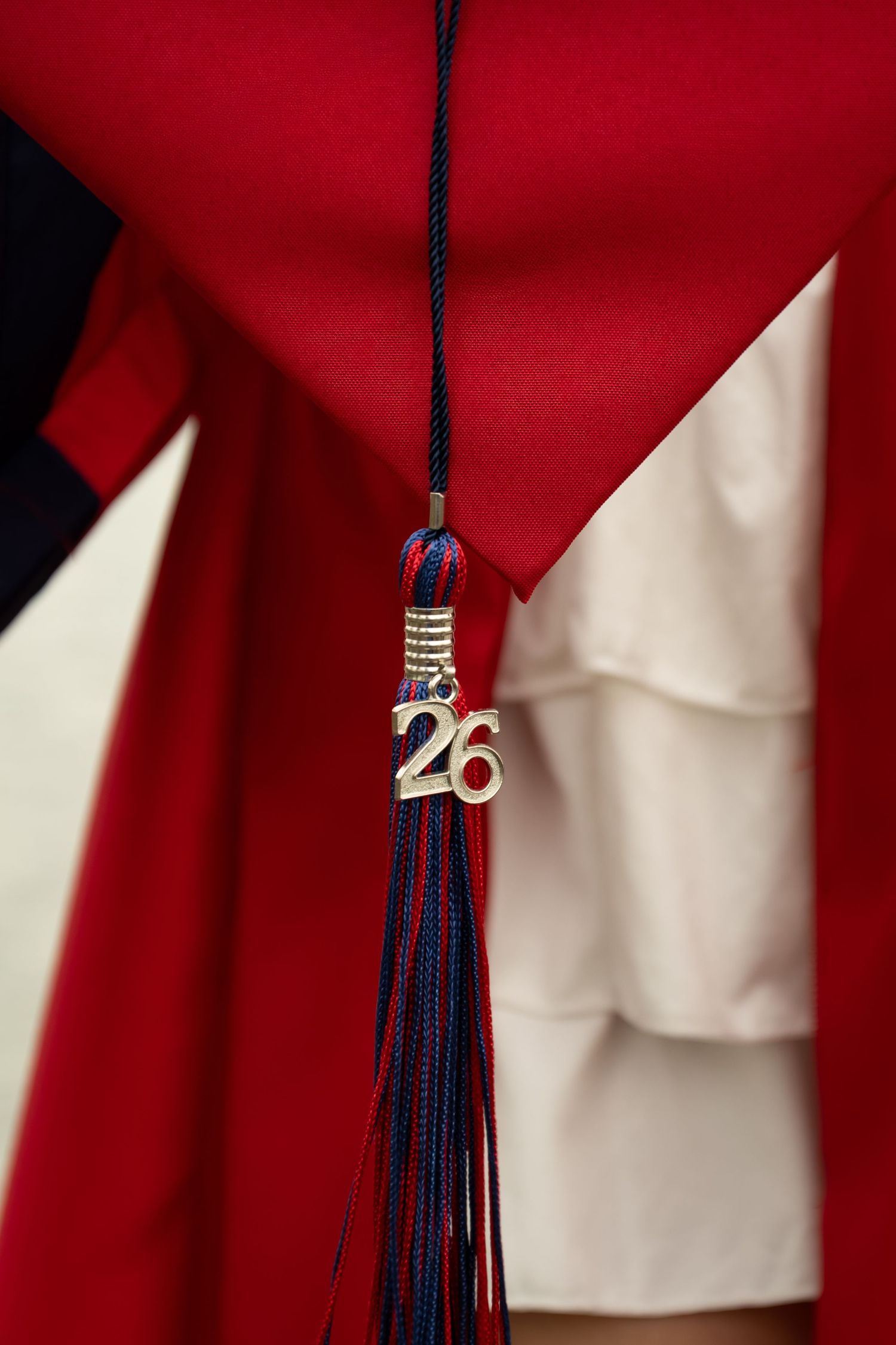 Close-up of a graduation tassel with gold '26' charm on red academic gown for class of 2026.
