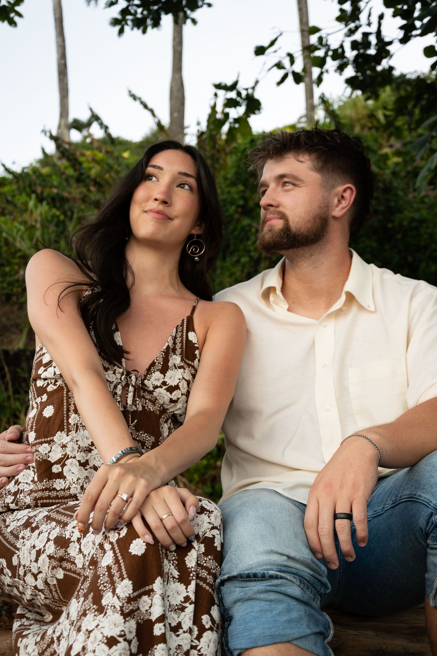 A couple in casual attire sits close together outdoors sharing intimate moments in a romantic photoshoot series.