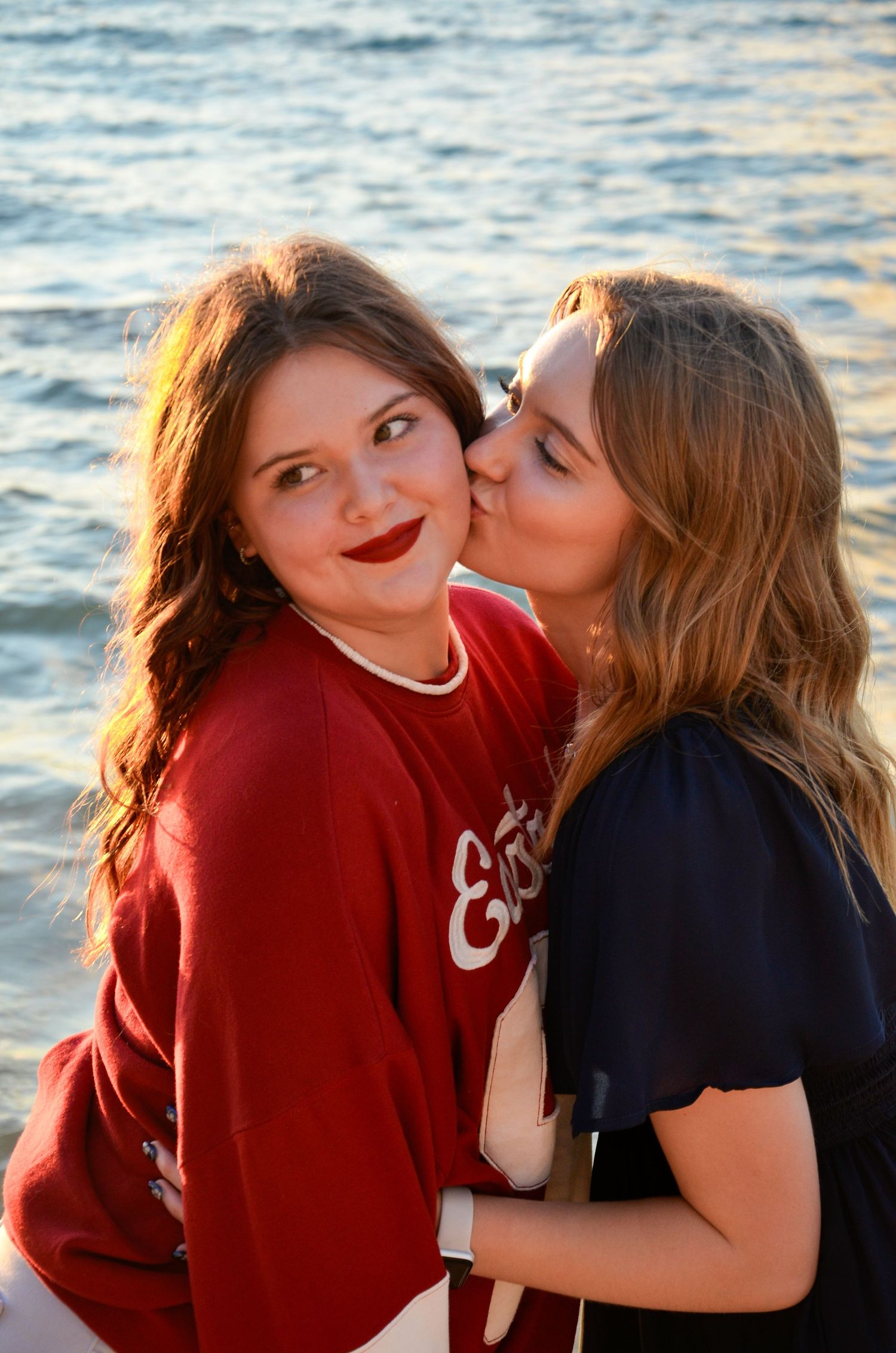 Two sisters sharing affectionate moment by the ocean at sunset.