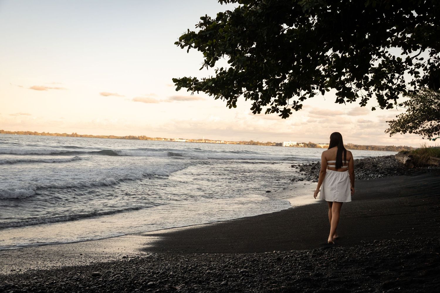 A person walks along a scenic beach shoreline at sunset with waves rolling onto the sand.