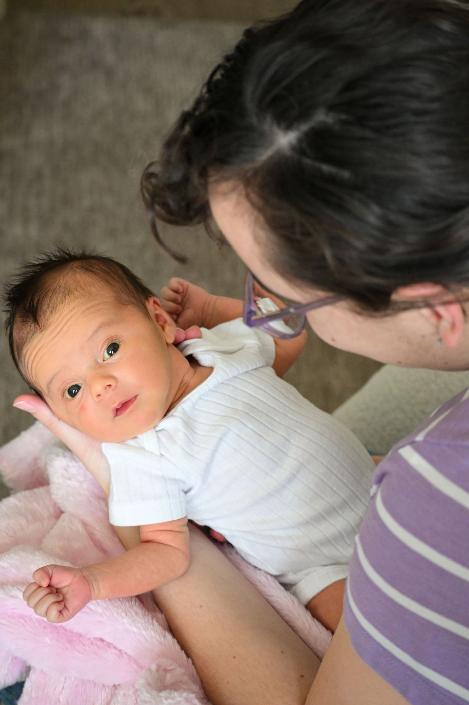 Infant in white onesie lying on pink blanket looking up attentively.