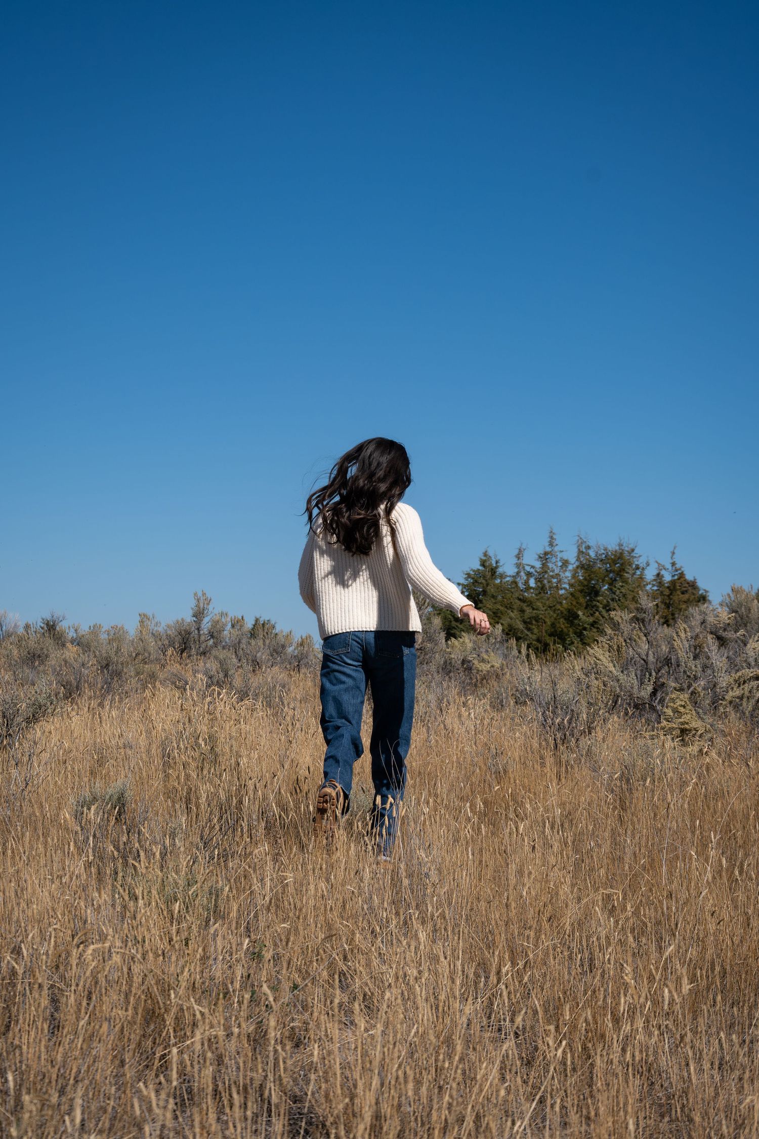 Person walking uphill through tall dry grass on a sunny day against bright blue sky.