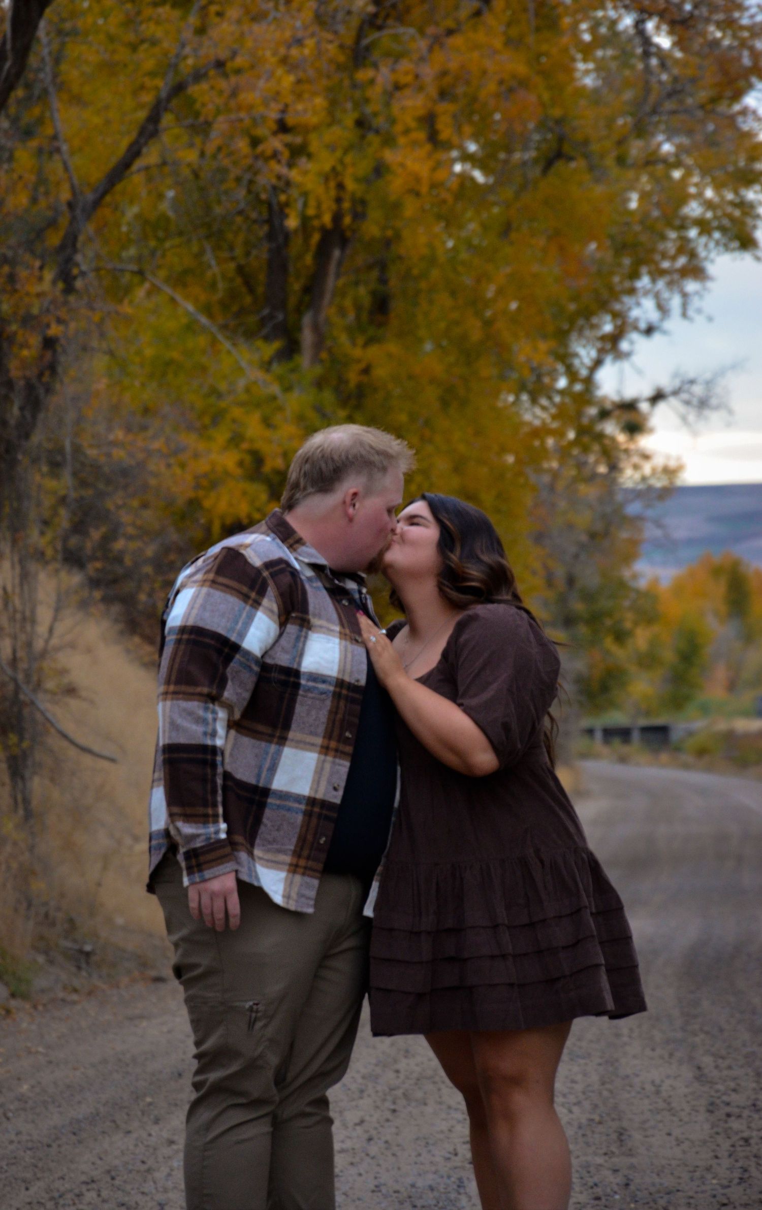 Romantic autumn portrait on a dirt road with fall foliage in the background.