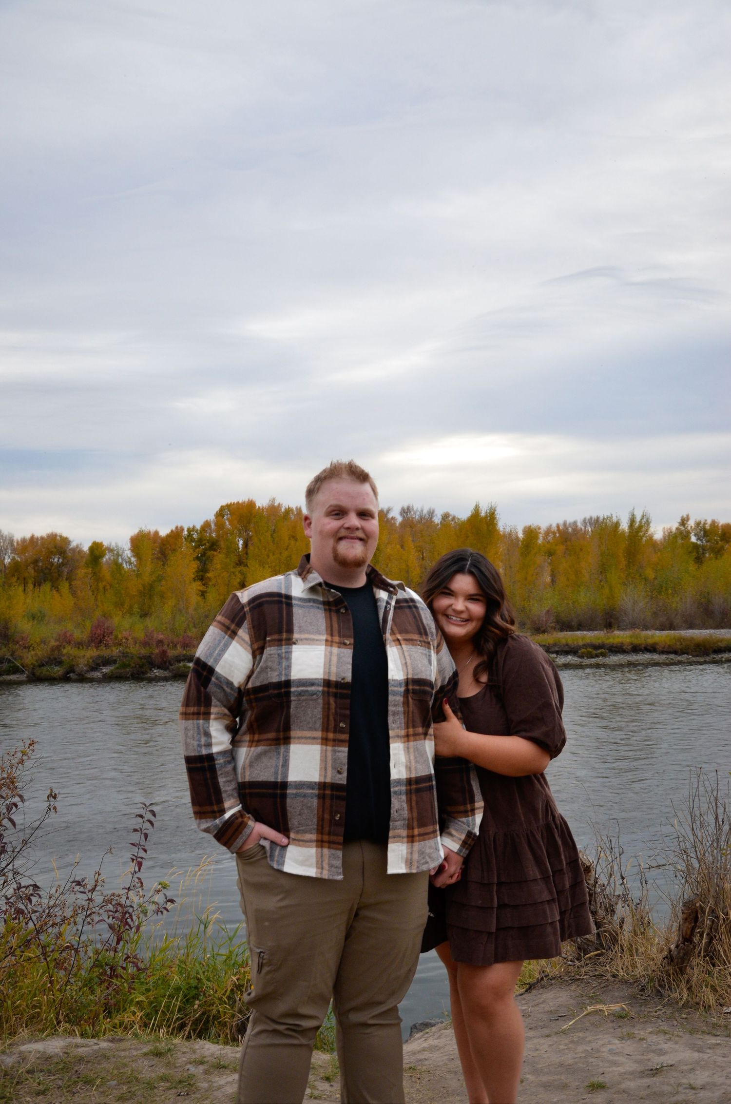 Casual couple portrait by a river with fall foliage in the background.