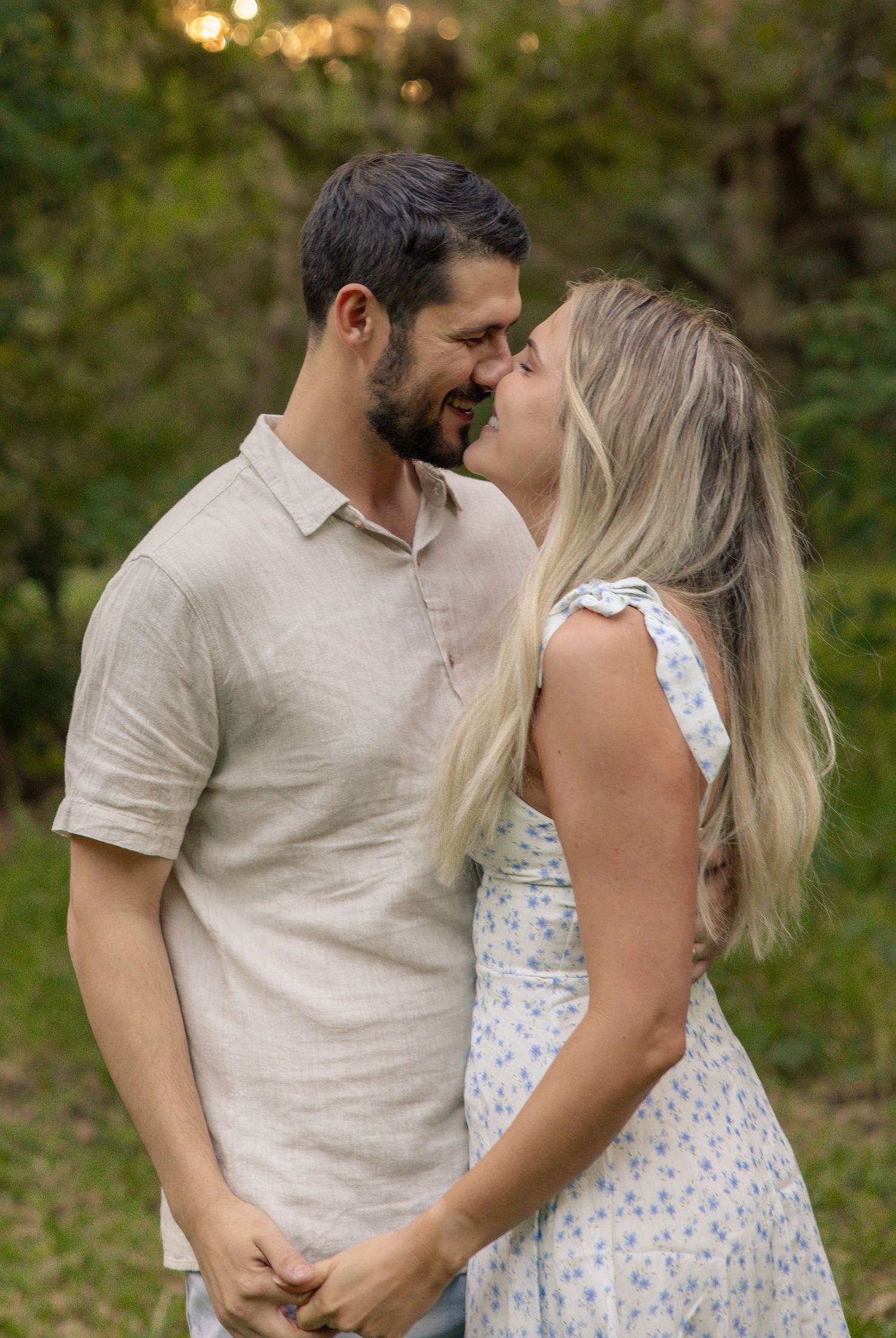 A couple in casual summer attire share an intimate moment while embracing in a sunlit outdoor setting.