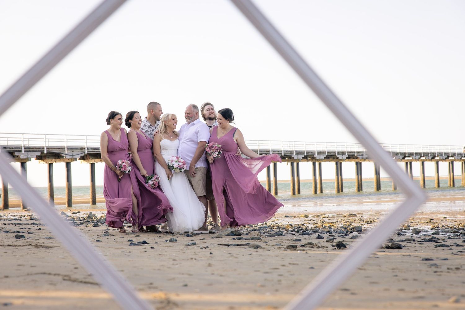 Family group sitting together on a beach at sunset with a pier visible in the background.