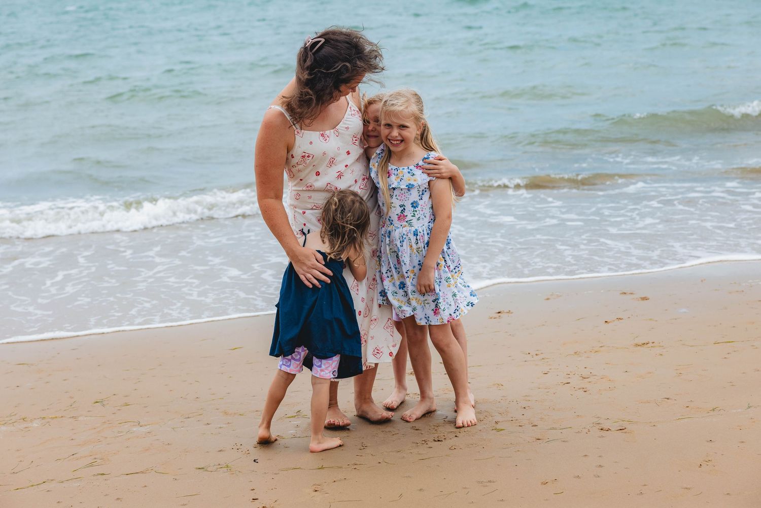 Family enjoying a moment together on a sunny beach with waves in the background.