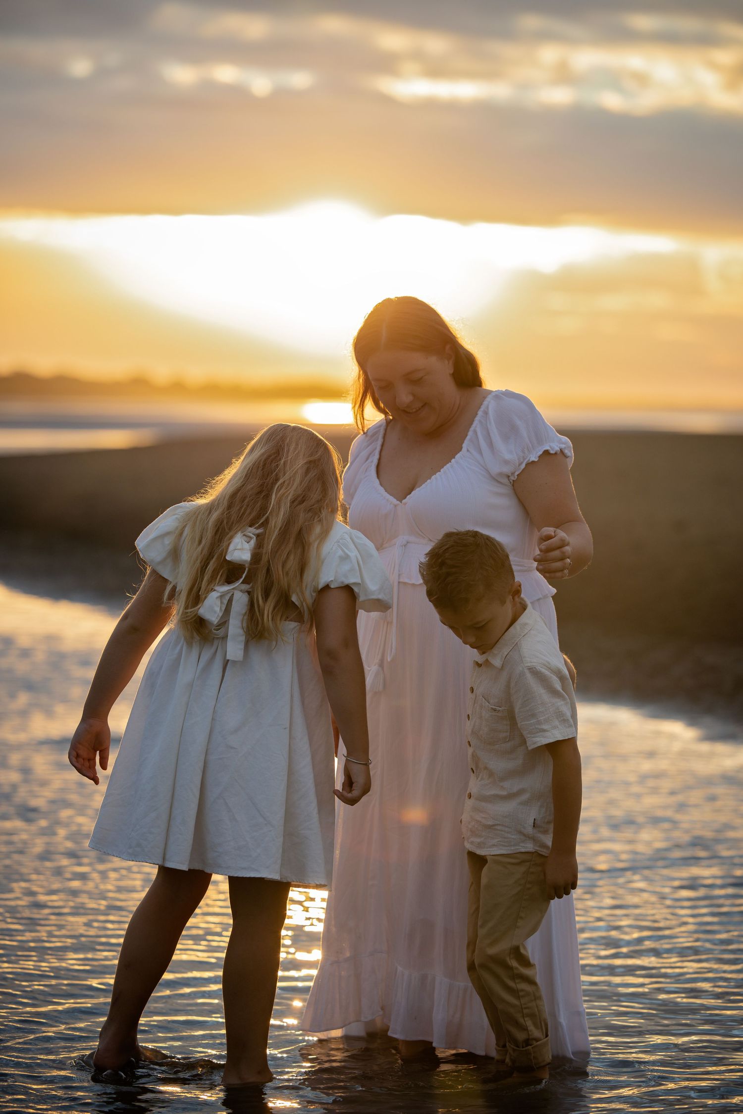 A family stands together on a beach at sunset with sunlight streaming through clouds and reflecting on wet sand.