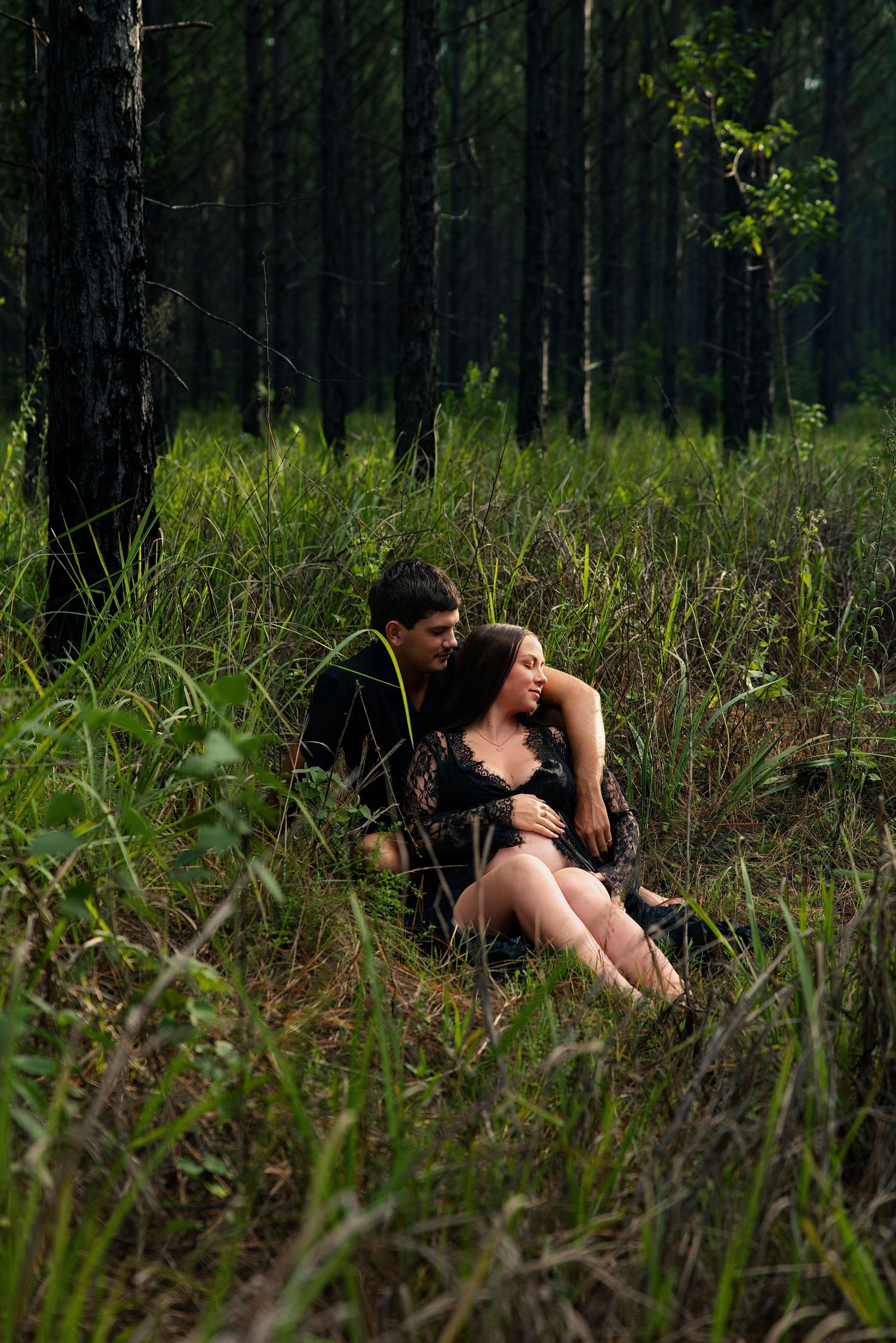 Person lying in tall grass at the edge of a dark forest on a sunny day.