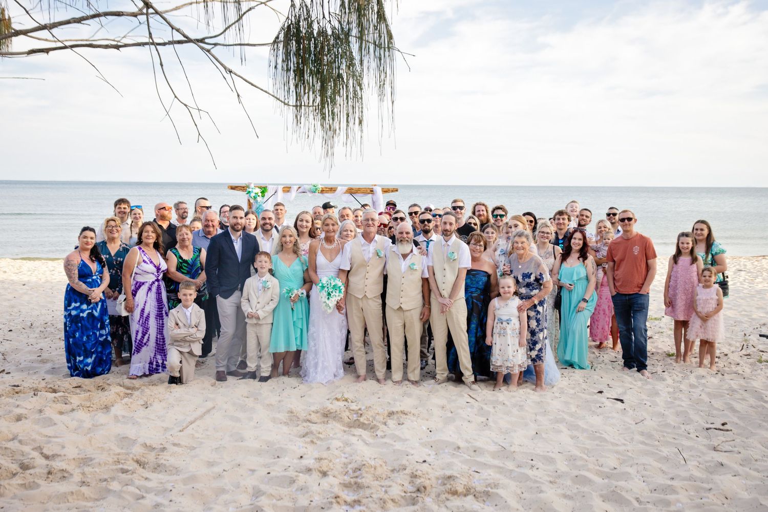 Wedding party group photos on a beach with guests wearing pastel colors and formal attire.