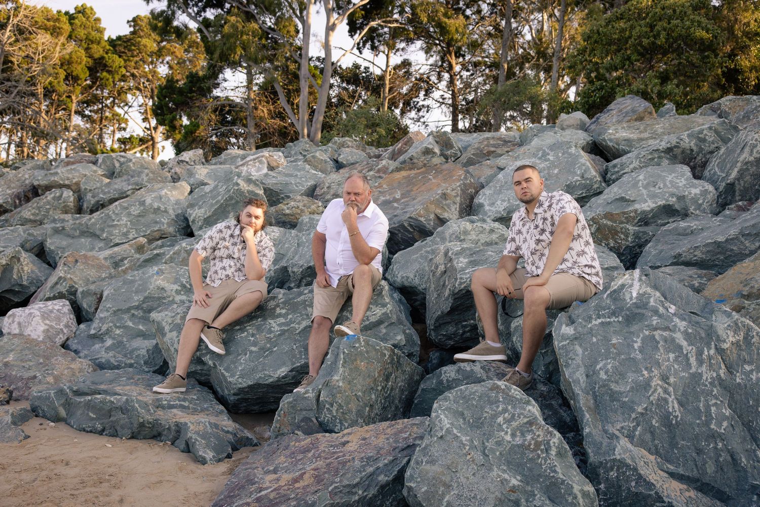 A couple poses together on large coastal rocks at sunset with trees visible in the background.