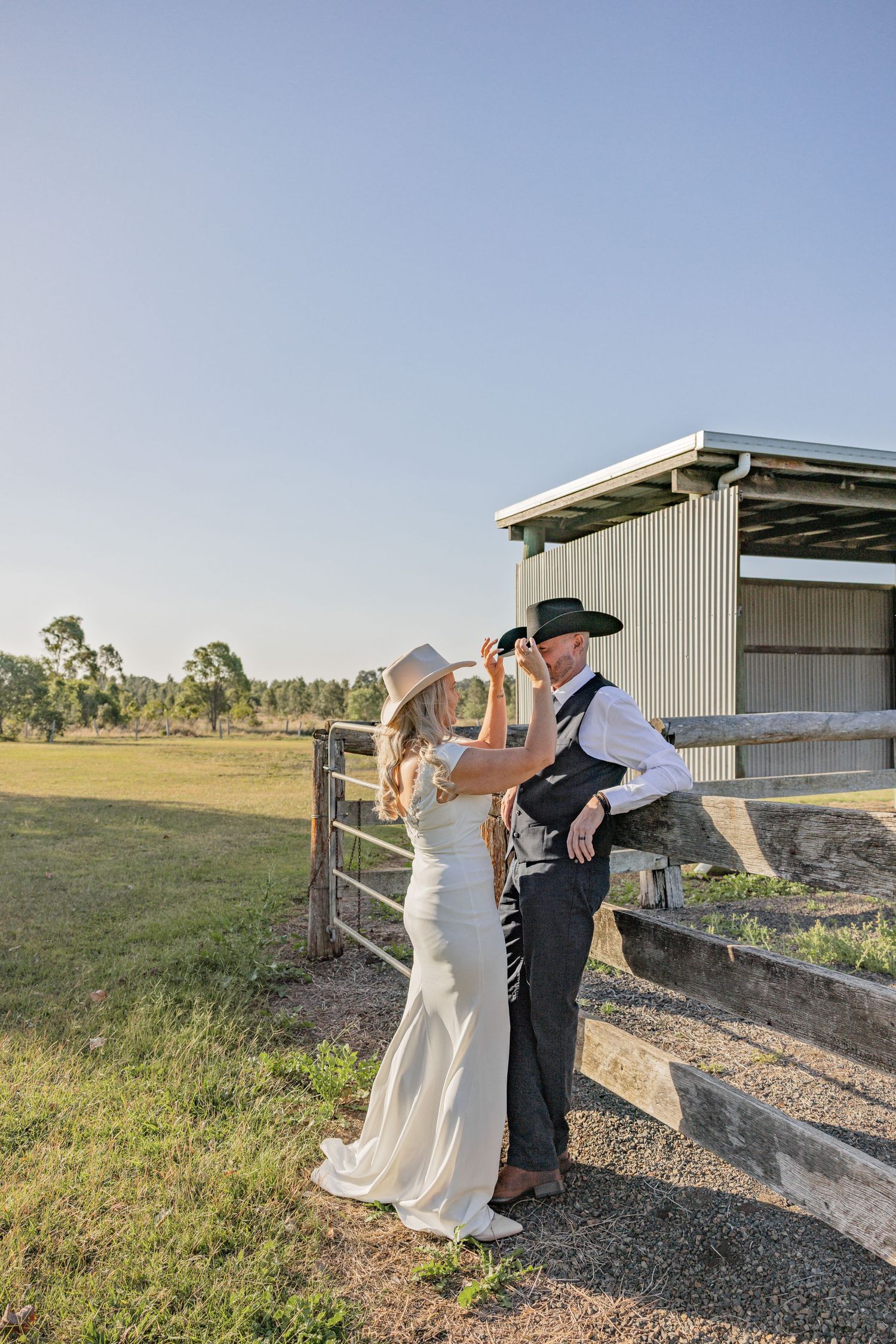 A couple in wedding attire dips gracefully in a romantic dance pose against a rustic countryside backdrop at sunset.