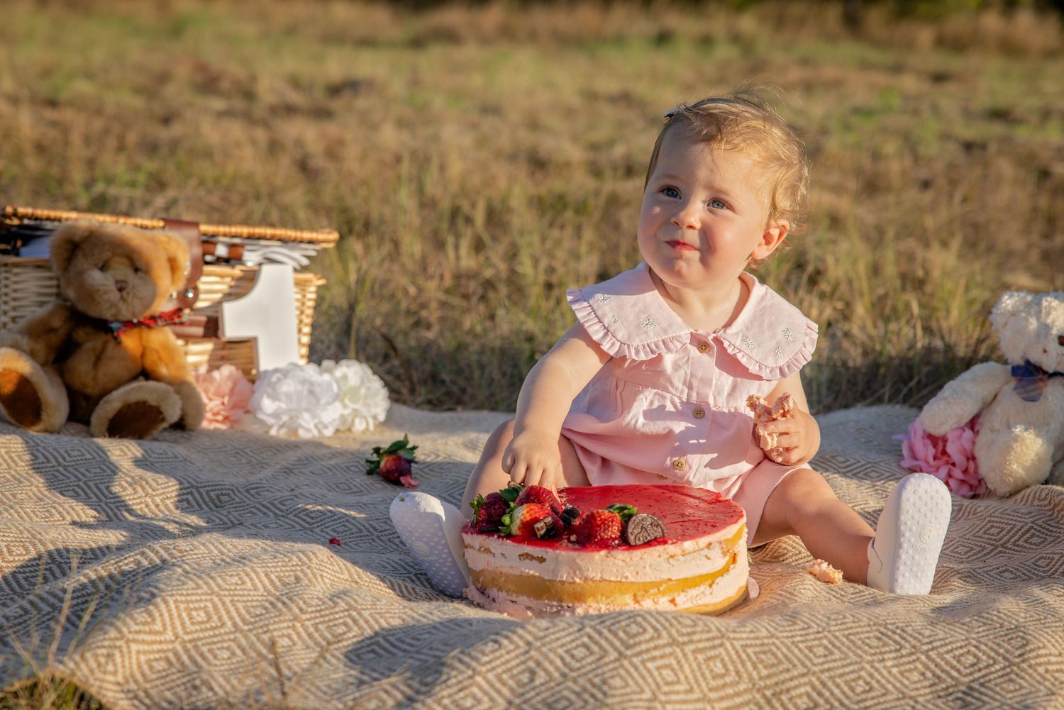 Picnic blanket on grassy terrain with food and drinks spread out during golden hour sunset.