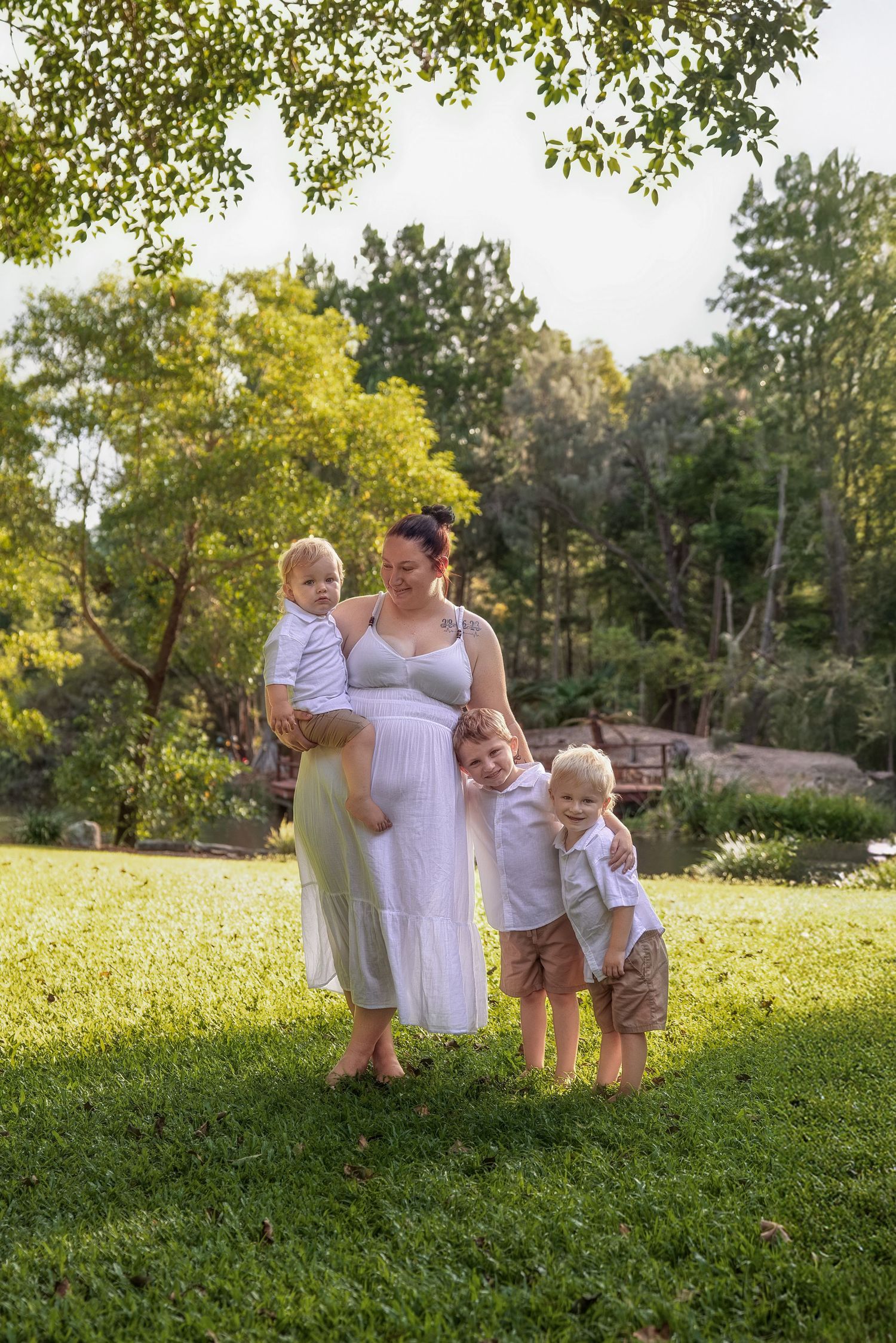 Family wearing white and blue outfits poses together on a grassy hill during golden hour in a park setting.