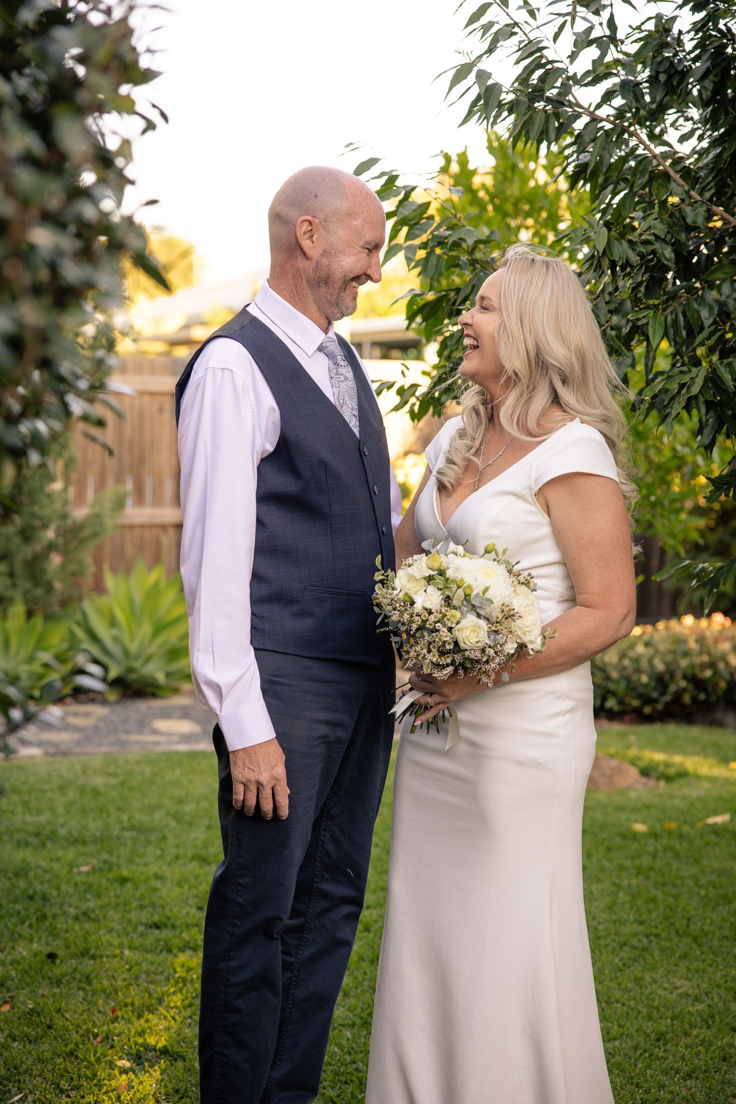 A couple shares a joyful moment in a garden setting during their wedding celebration, surrounded by greenery.