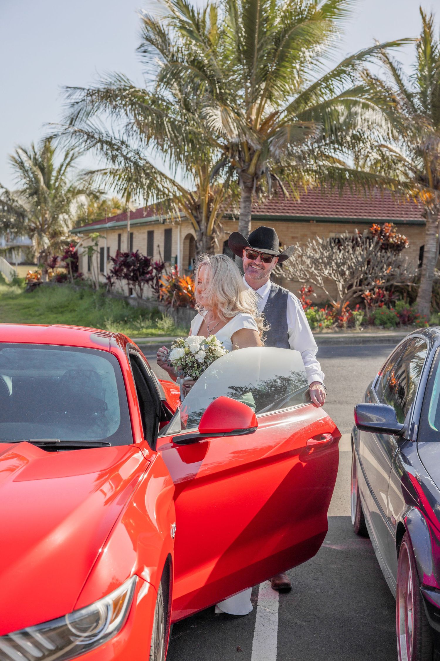 A bright red Ferrari sports car parked in front of palm trees with people gathered around to admire it.