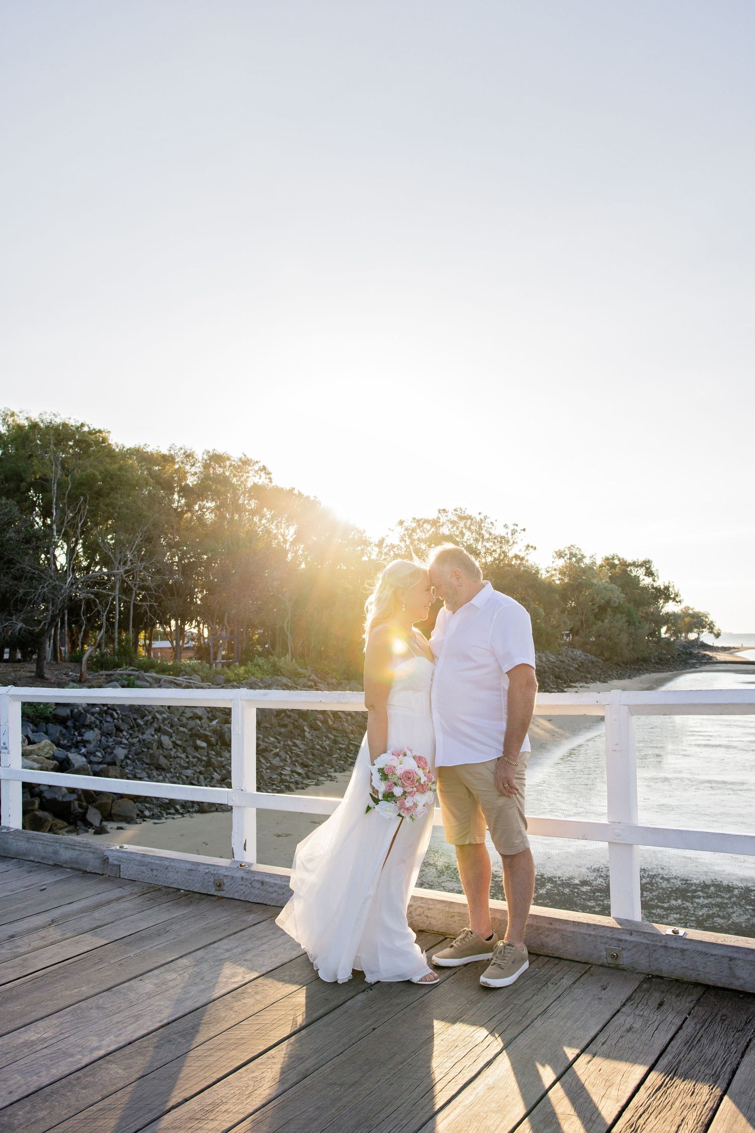 Romantic sunset moment on a wooden pier overlooking the water with golden sunlight streaming through the trees.
