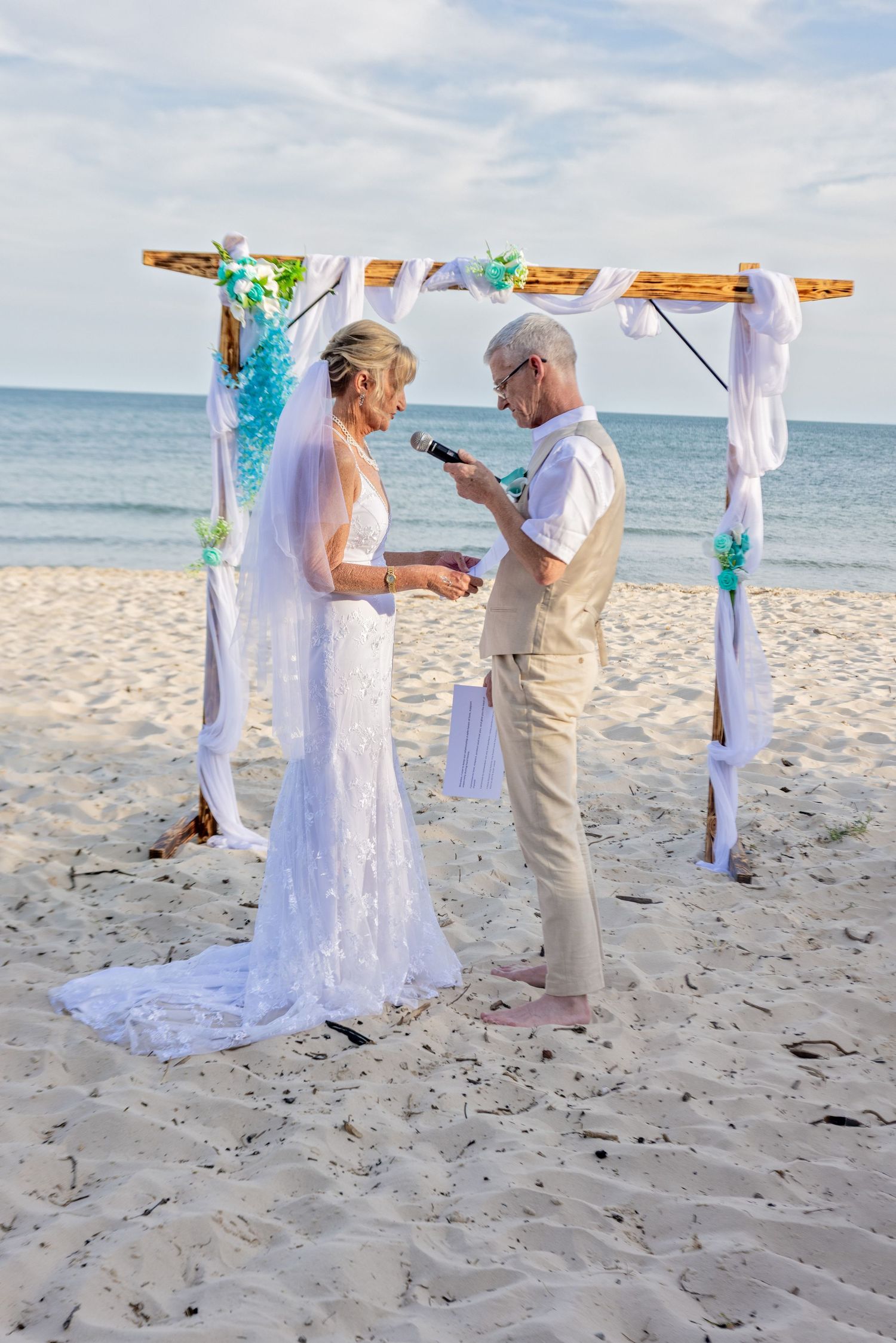 A beach wedding ceremony taking place on white sand with turquoise ocean waters visible in the background.